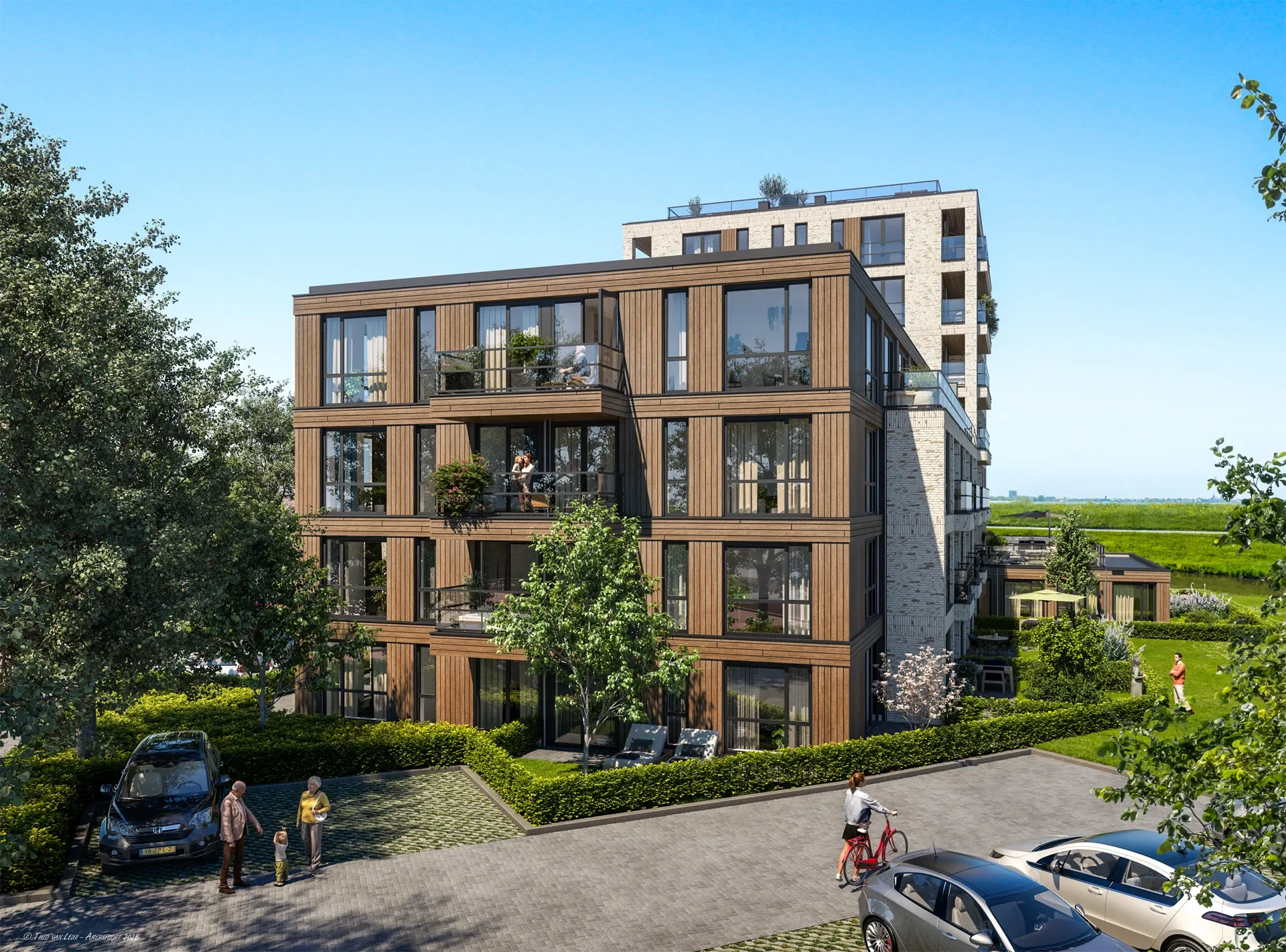 Een modern meerlaag appartementencomplex met grote ramen en balkons, omgeven door groene tuinen en een parkeerplaats, in een landelijke omgeving onder een heldere blauwe hemel.