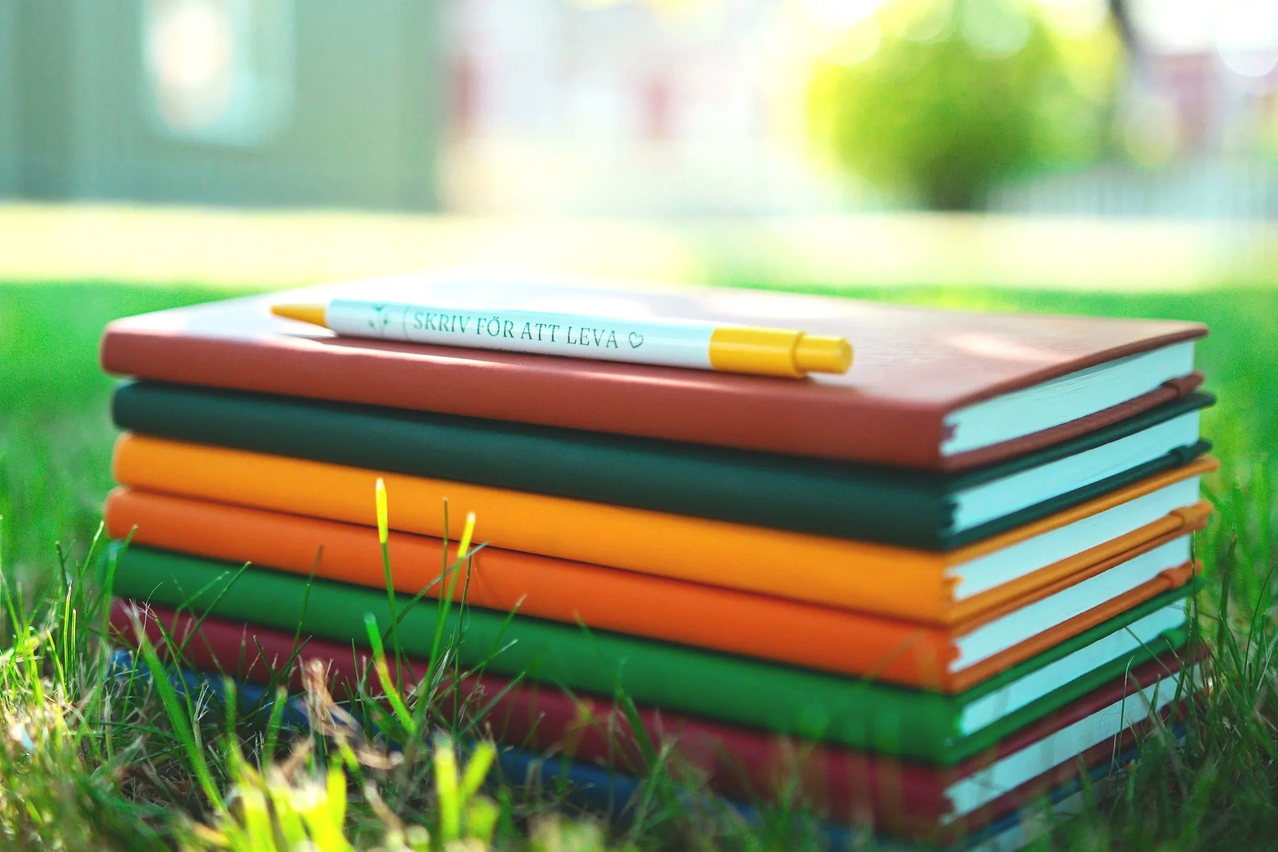 En hög med färgglada böcker och en penna från skrivkursen med Skriv för att leva