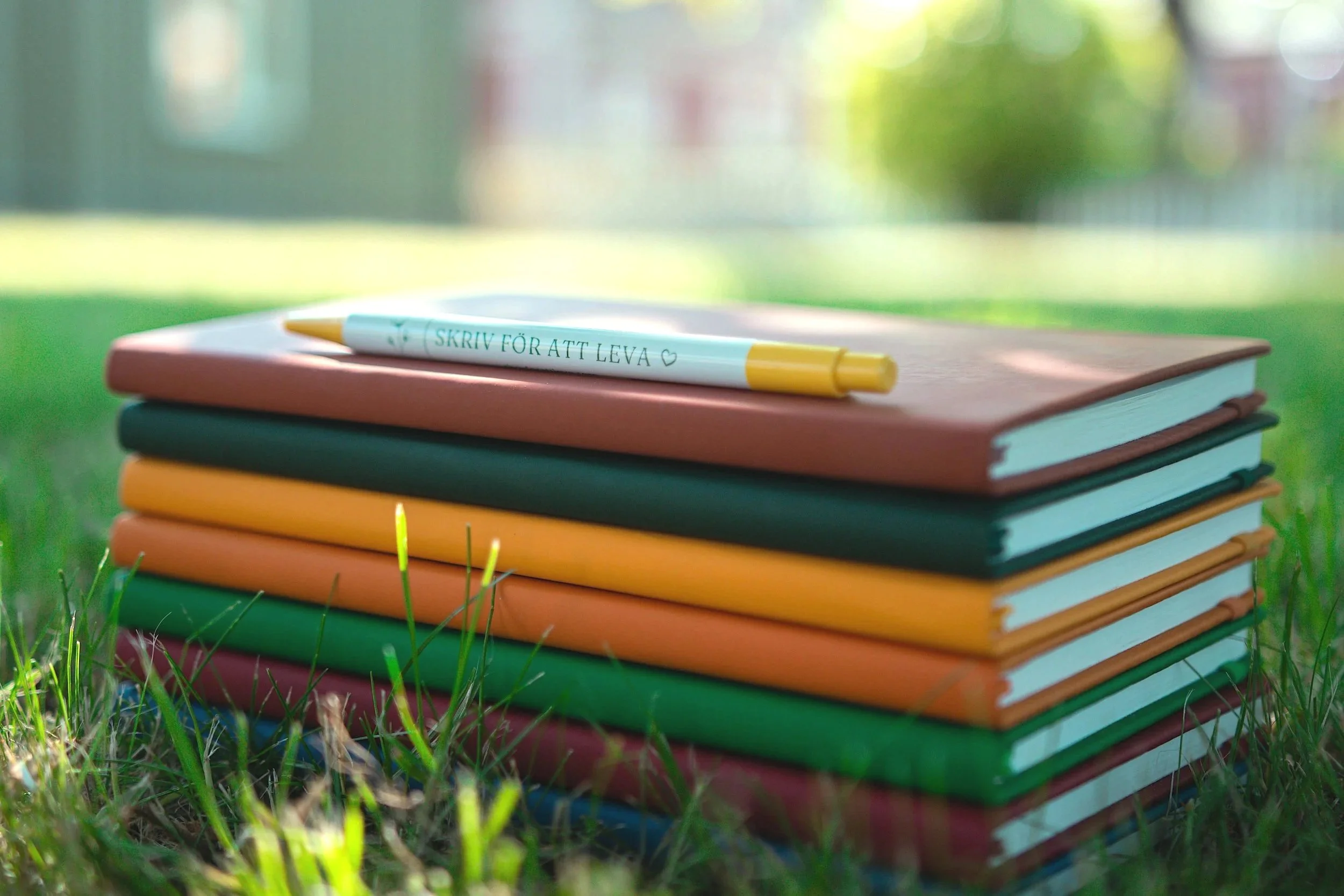 En hög med färgglada skrivböcker och en penna från Skriv för att leva