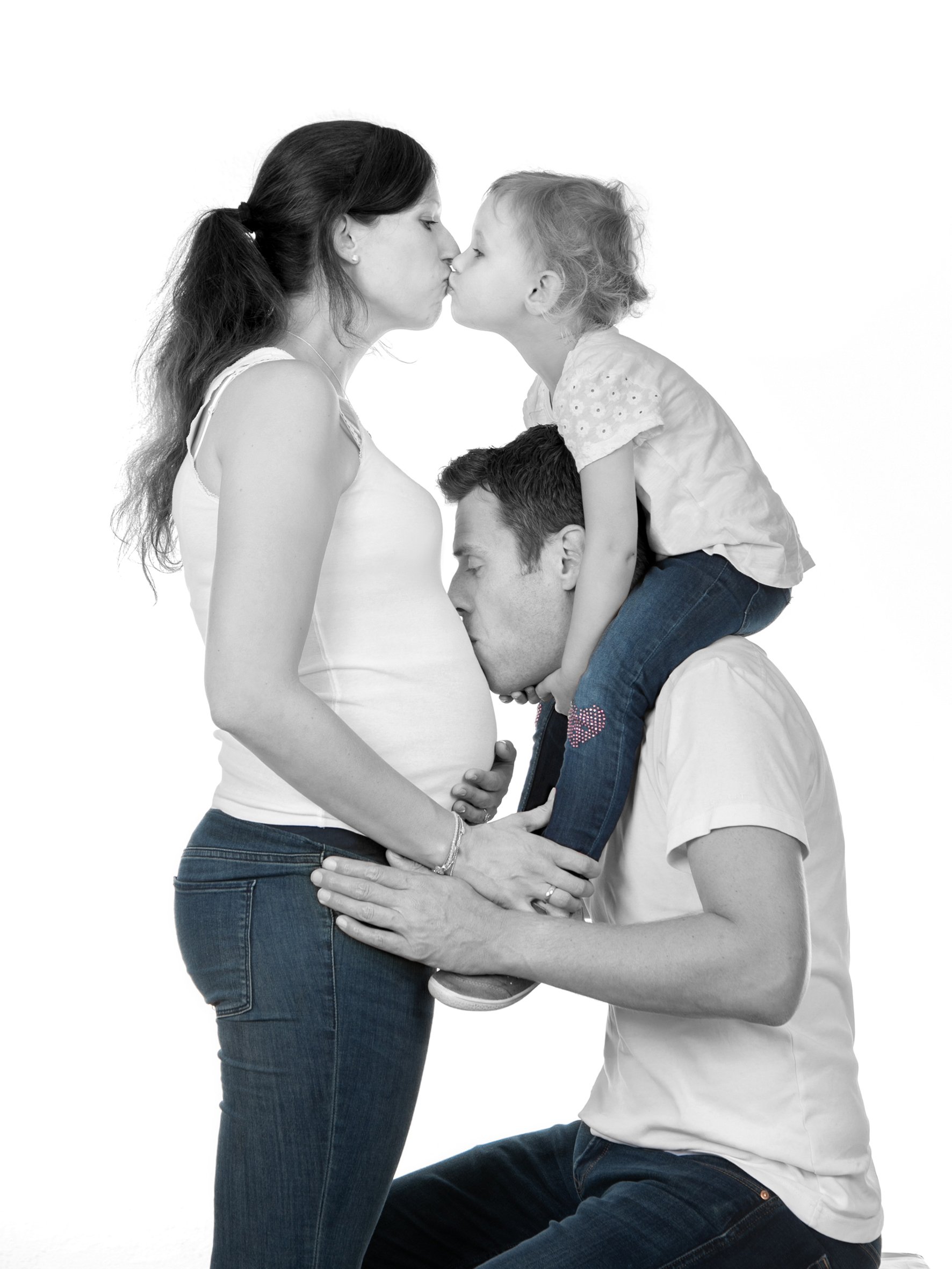 Familie mit schwangerer Mutter, die von Vater und Kind umarmt und küsst wird.