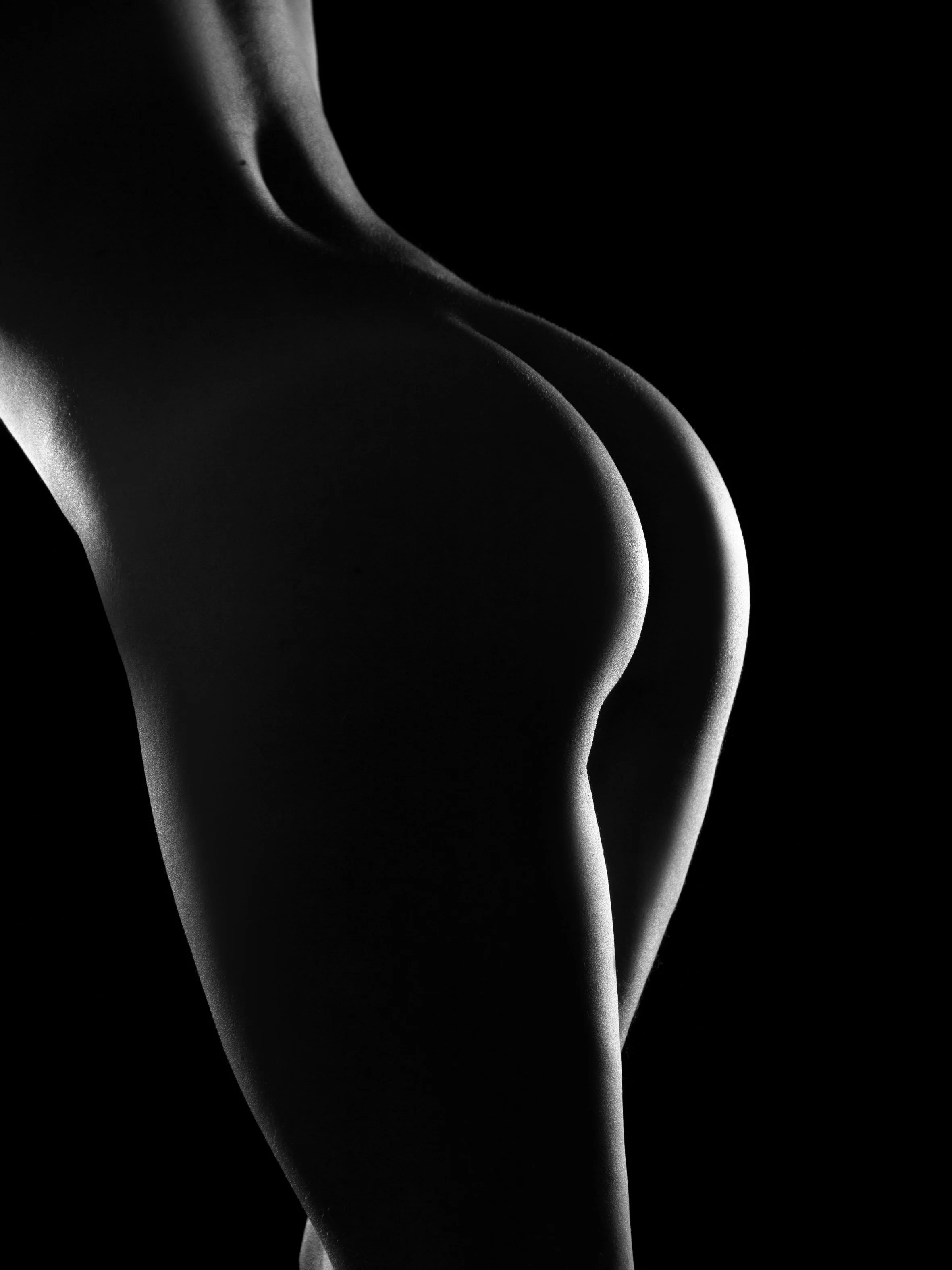 Schwarz-Weiß-Foto einer menschlichen Oberschenkel- und Gesäßkontur mit dramatischer Beleuchtung.