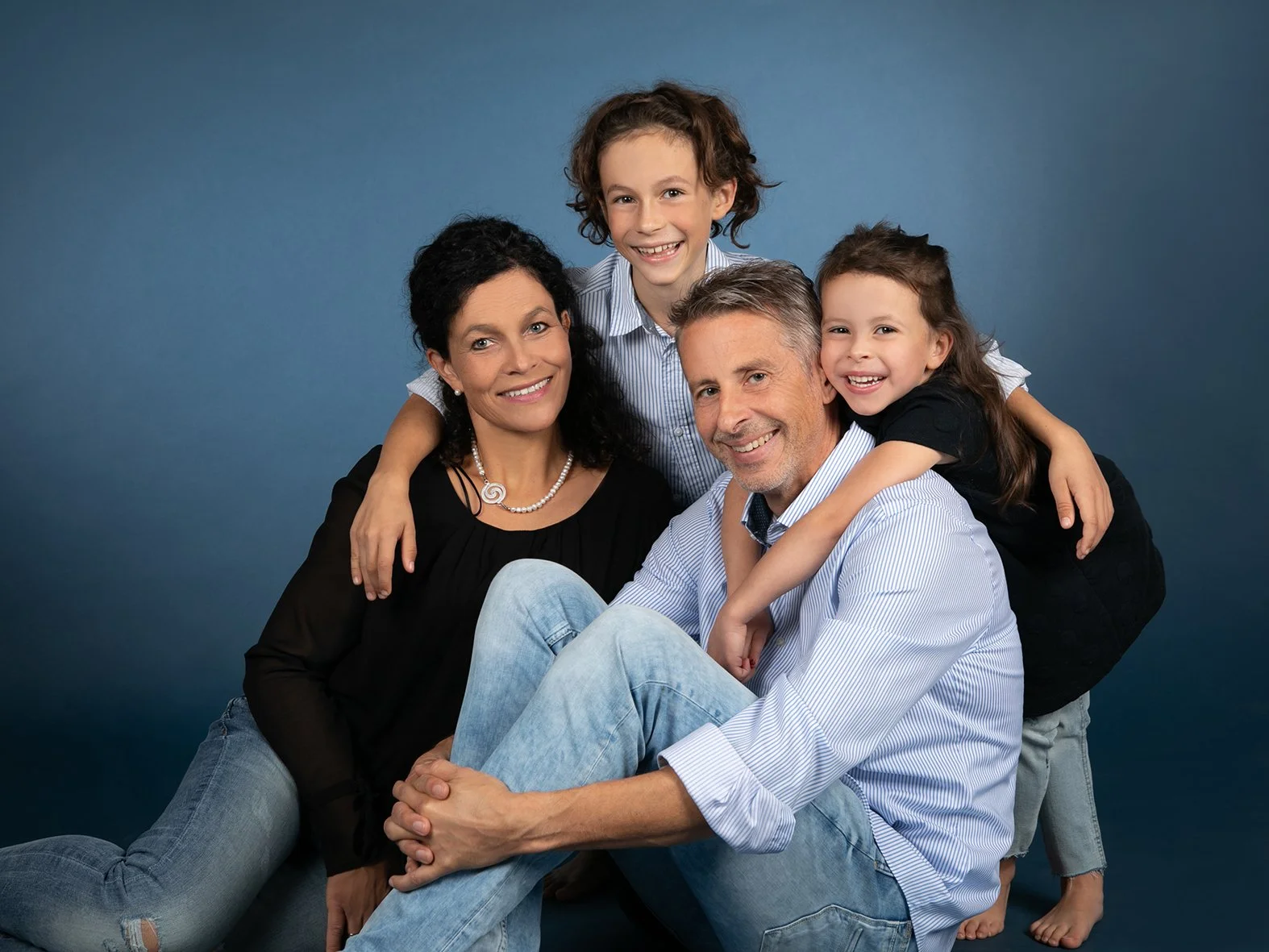 Eine lachende Familie, bestehend aus einem Mann, einer Frau und zwei Kindern, posiert vor blauem Hintergrund.