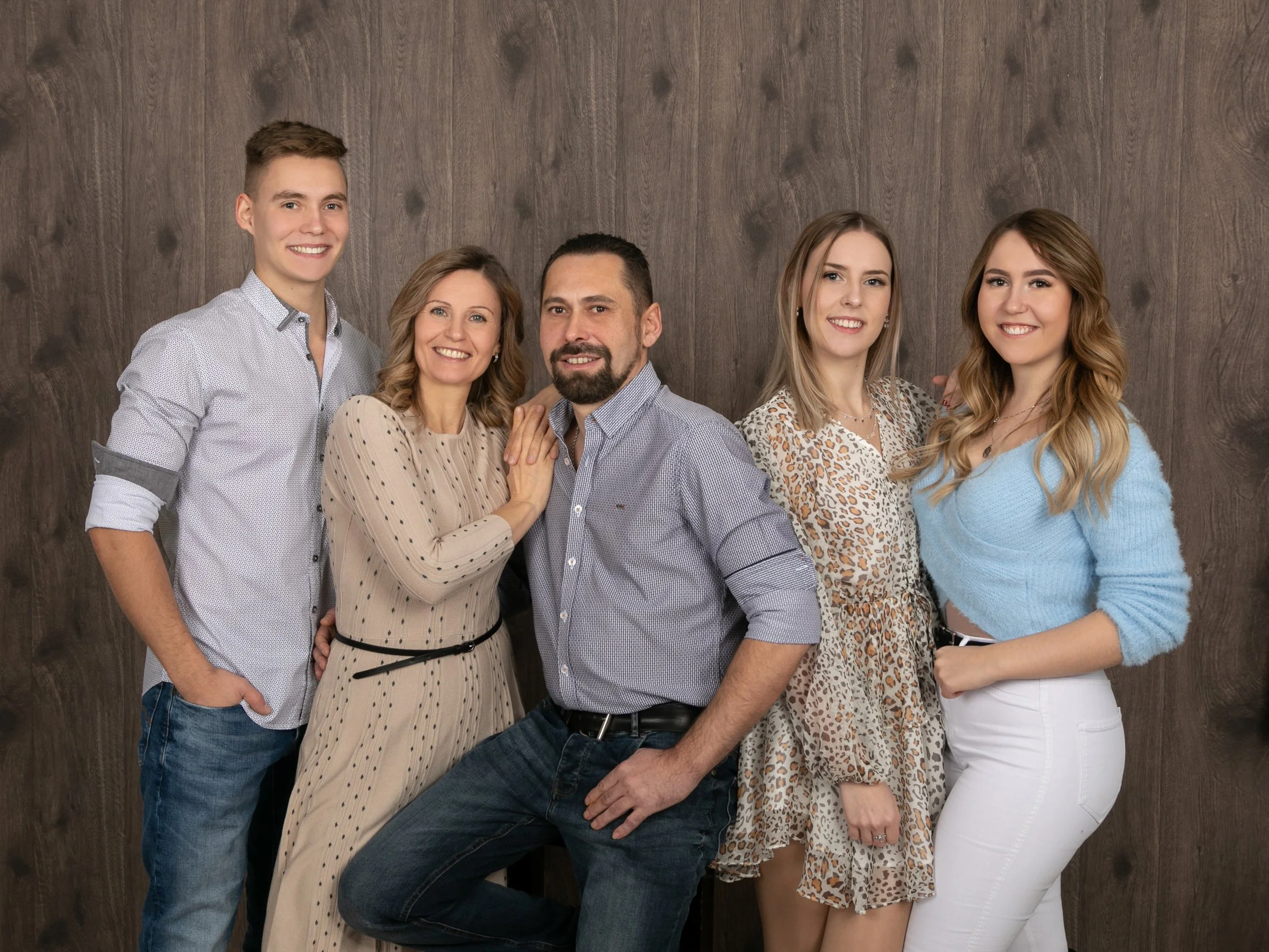 Sechs Menschen posieren vor einer Holzwand für ein Gruppenfoto, lächeln.