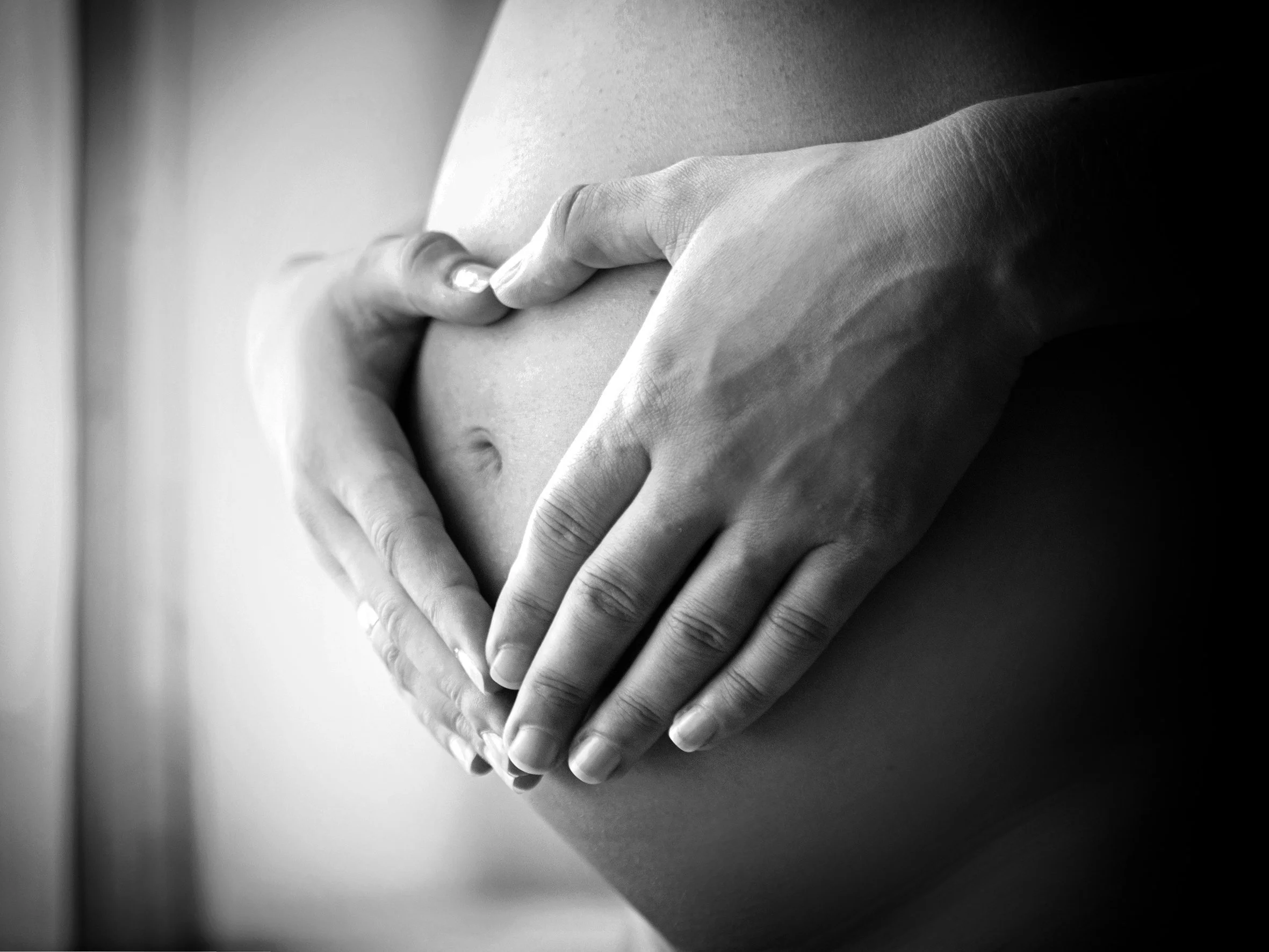 Schwarz-weiß-Foto von einer Person, die ihre Hände auf ihren Bauch legt, vermutlich eine schwangere Frau.