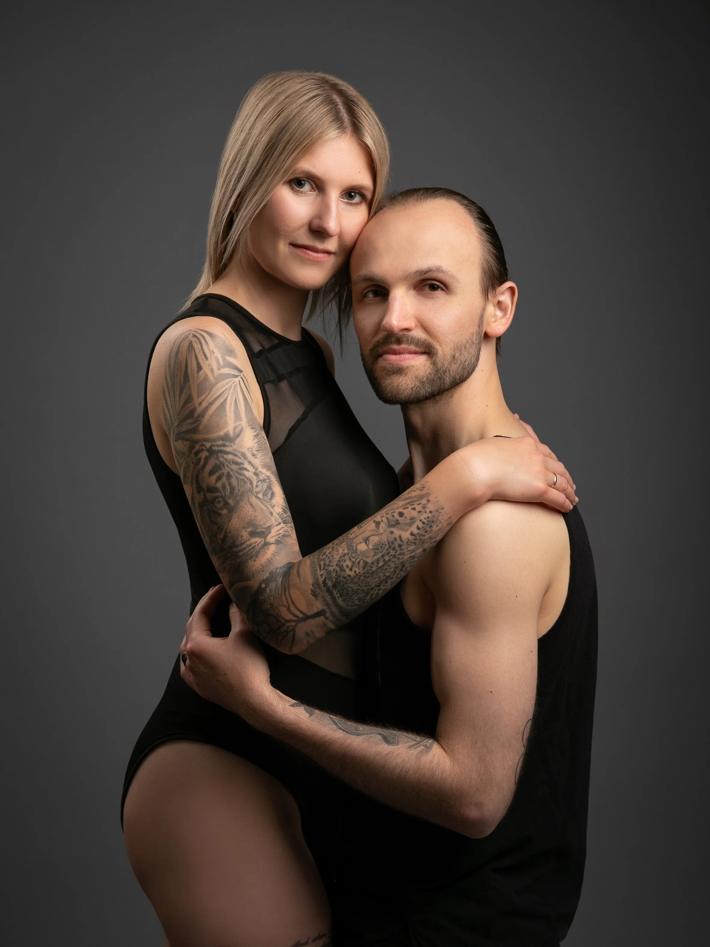 Ein Mann und eine Frau stehen eng zusammen. Sie umarmen sich und schauen in die Kamera. Der Hintergrund ist grau.