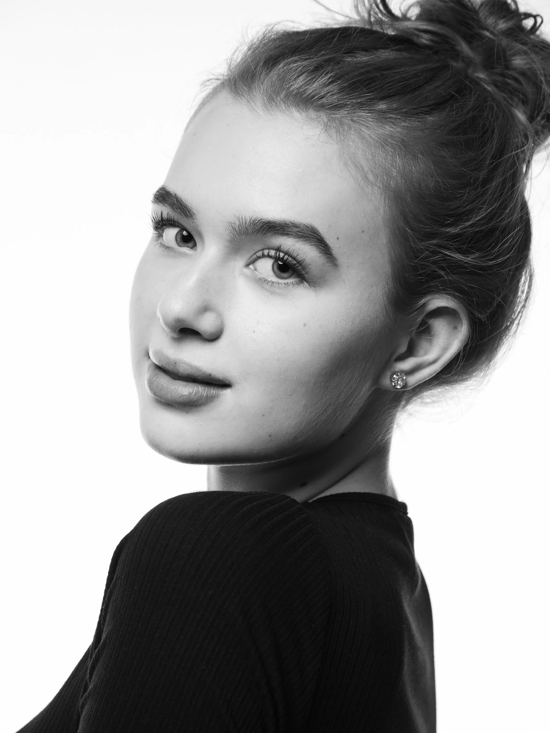 Schwarz-weiß Porträt einer jungen Frau mit hochgestecktem Haar, sichtbarem Haut mit natürlichen Texturen, dezentem Lächeln und Ohrringen