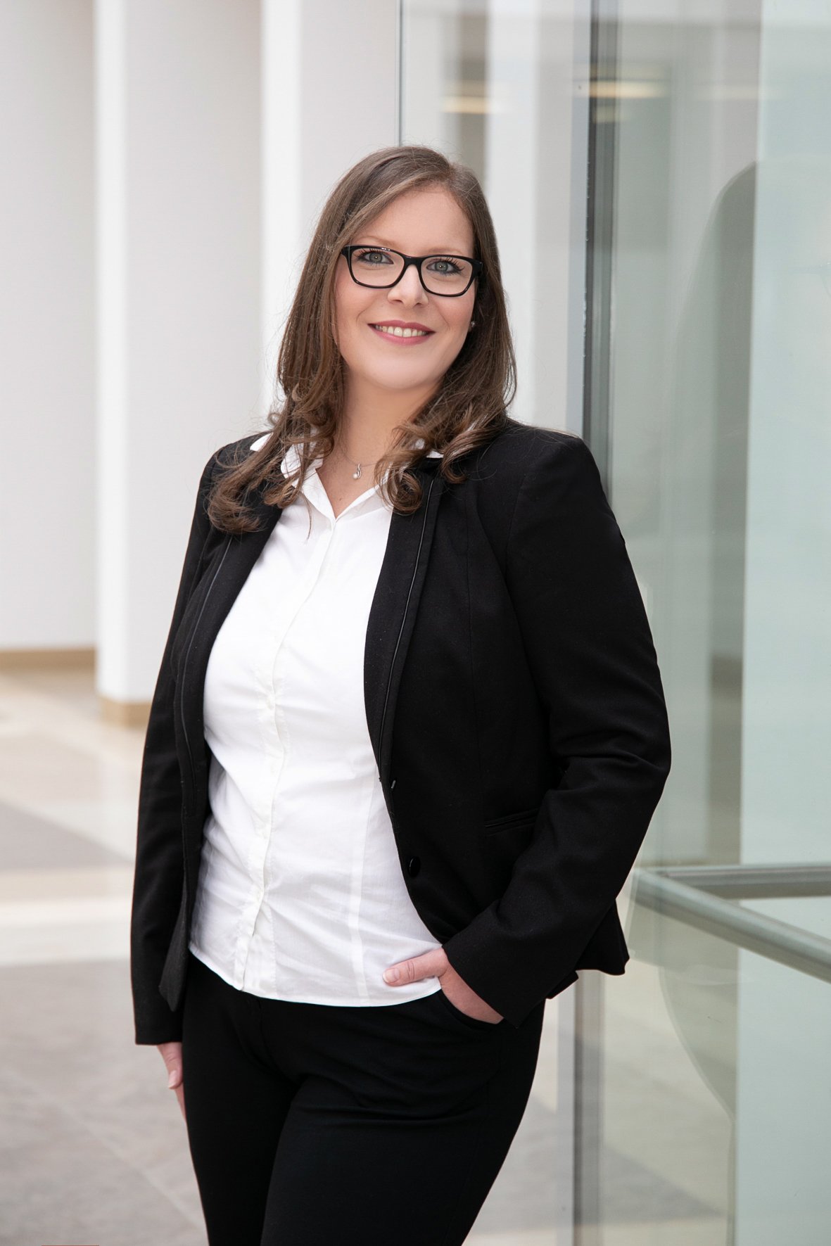 Eine professionelle Frau in einem Business-Anzug steht vor einem modernen Gebäude und lächelt in die Kamera.