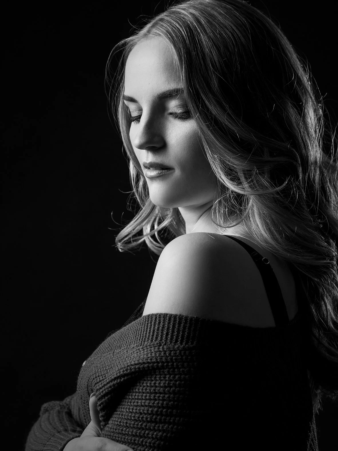 Schwarz-weiß-Foto eines lächelnden jungen Frau mit lockigem Haar, die die Augen geschlossen hat, in einem dunklen Raum