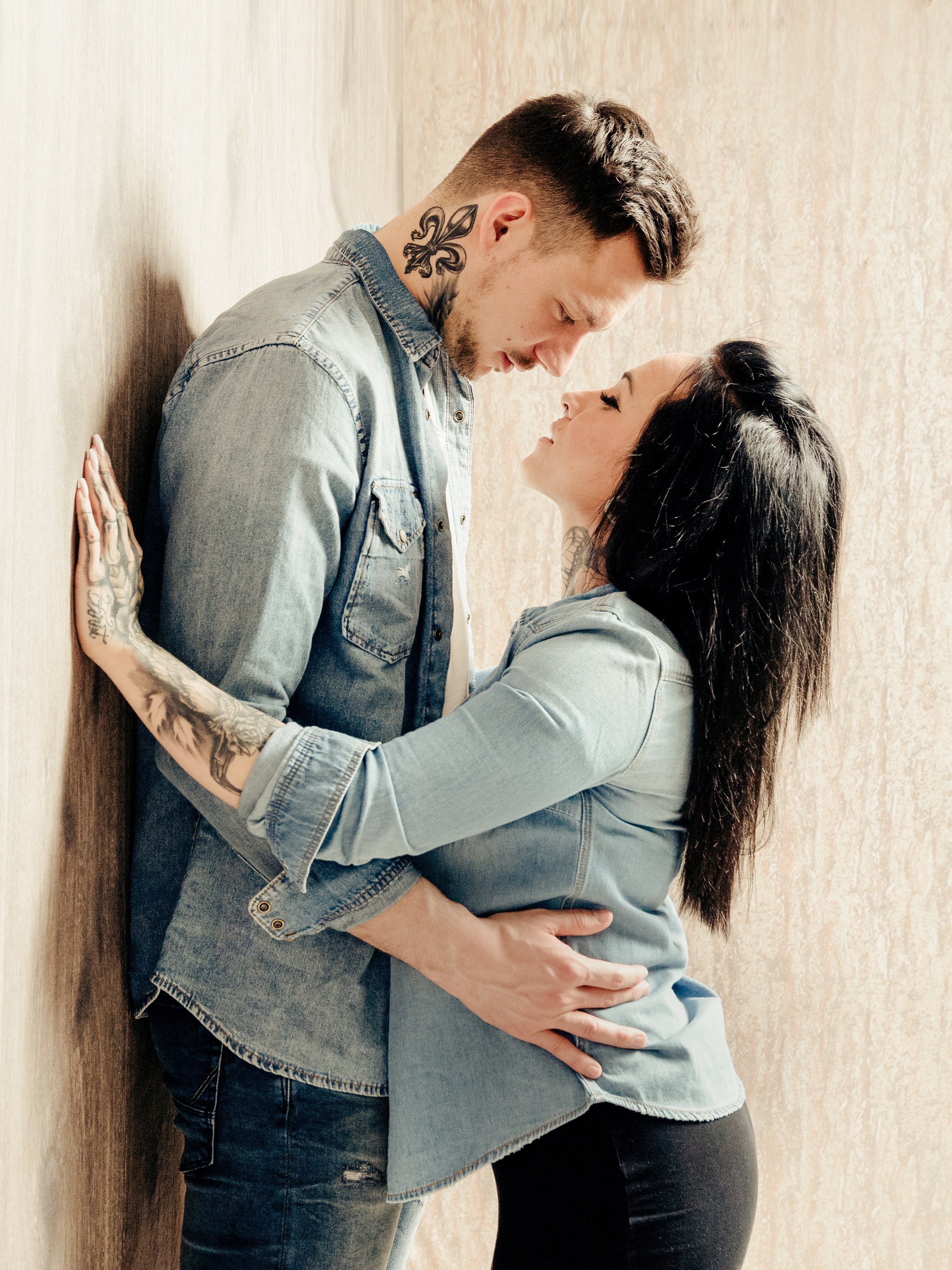 Ein Mann und eine Frau stehen dicht beieinander an einer Wand, sie schauen sich tief in die Augen und berühren sich zärtlich.
