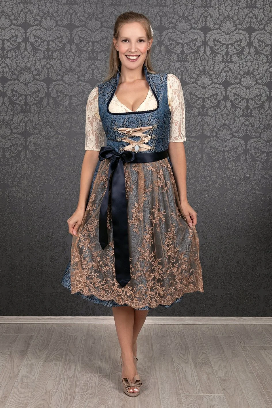 Eine junge Frau trägt ein traditionelles deutsches Dirndl mit blauer und goldener Verzierung und einem großen schwarzen Band um die Taille.