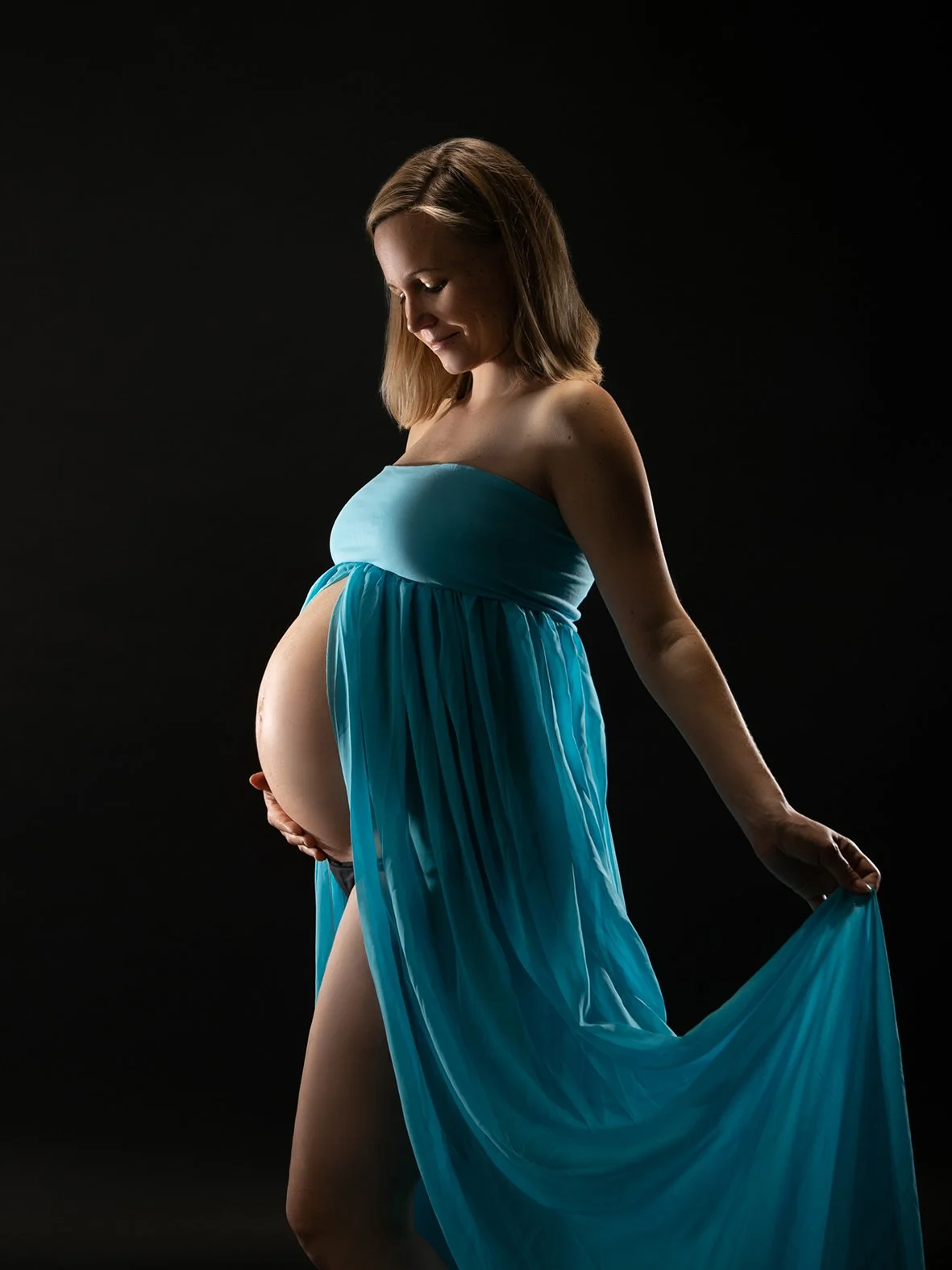 Schwangere Frau in Blaues Kleid vor schwarzem Hintergrund