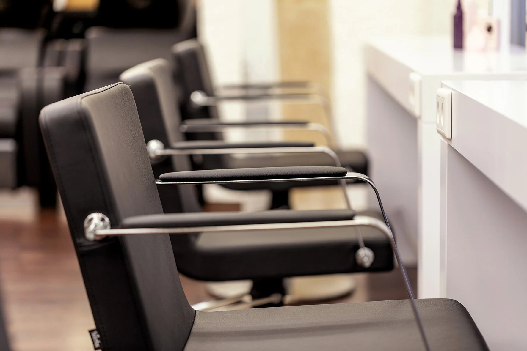 Leere schwarze Stühle in einem Wartebereich neben einer weißen Rezeption.