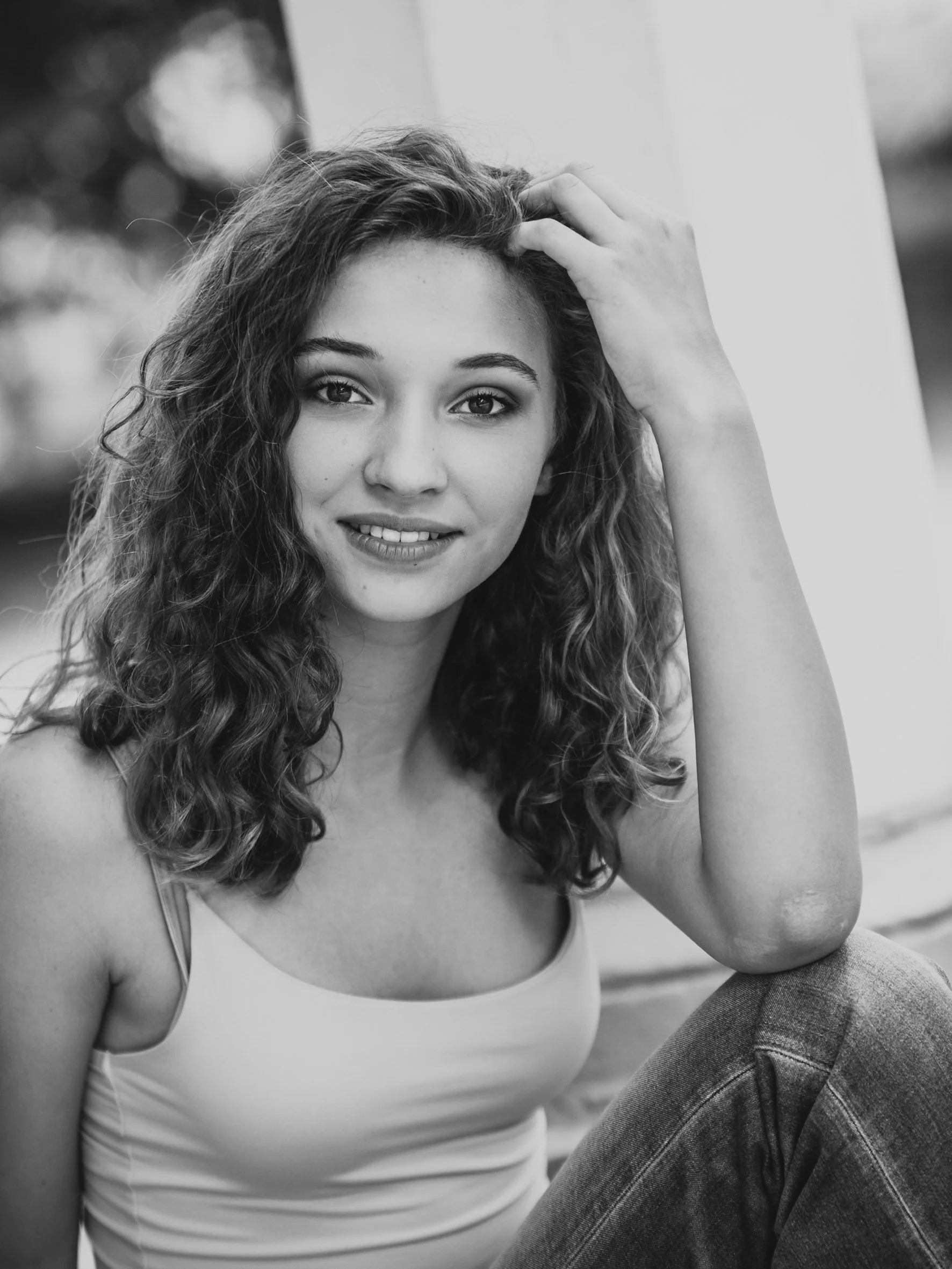 Schwarz-weiß Fotografie eines jungen Mädchens mit lockigem Haar, das lächelnd in die Kamera schaut.