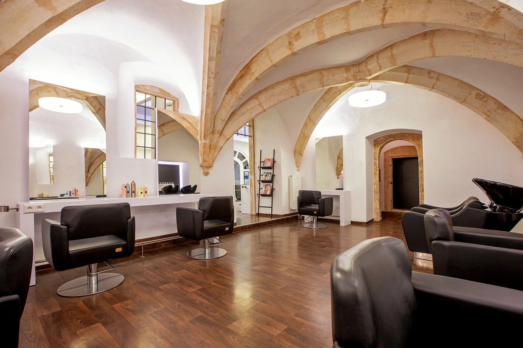 Ein Friseursalon mit schwarzen Haarsesseln, Holzfußboden und weißen Wänden mit mehreren Bögen.