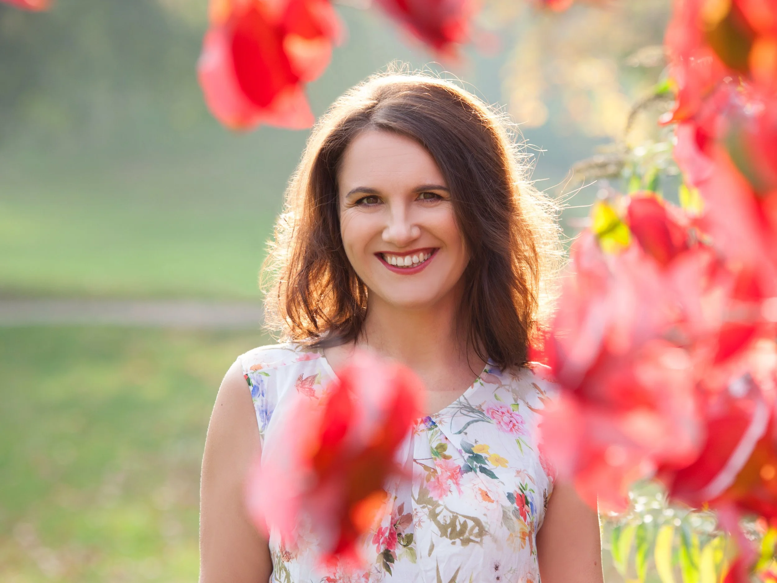 Lächelnde Frau im Sonnenschein, umgeben von roten Blumen, im Freien, bei Sonnenuntergang oder Sonnenaufgang.
