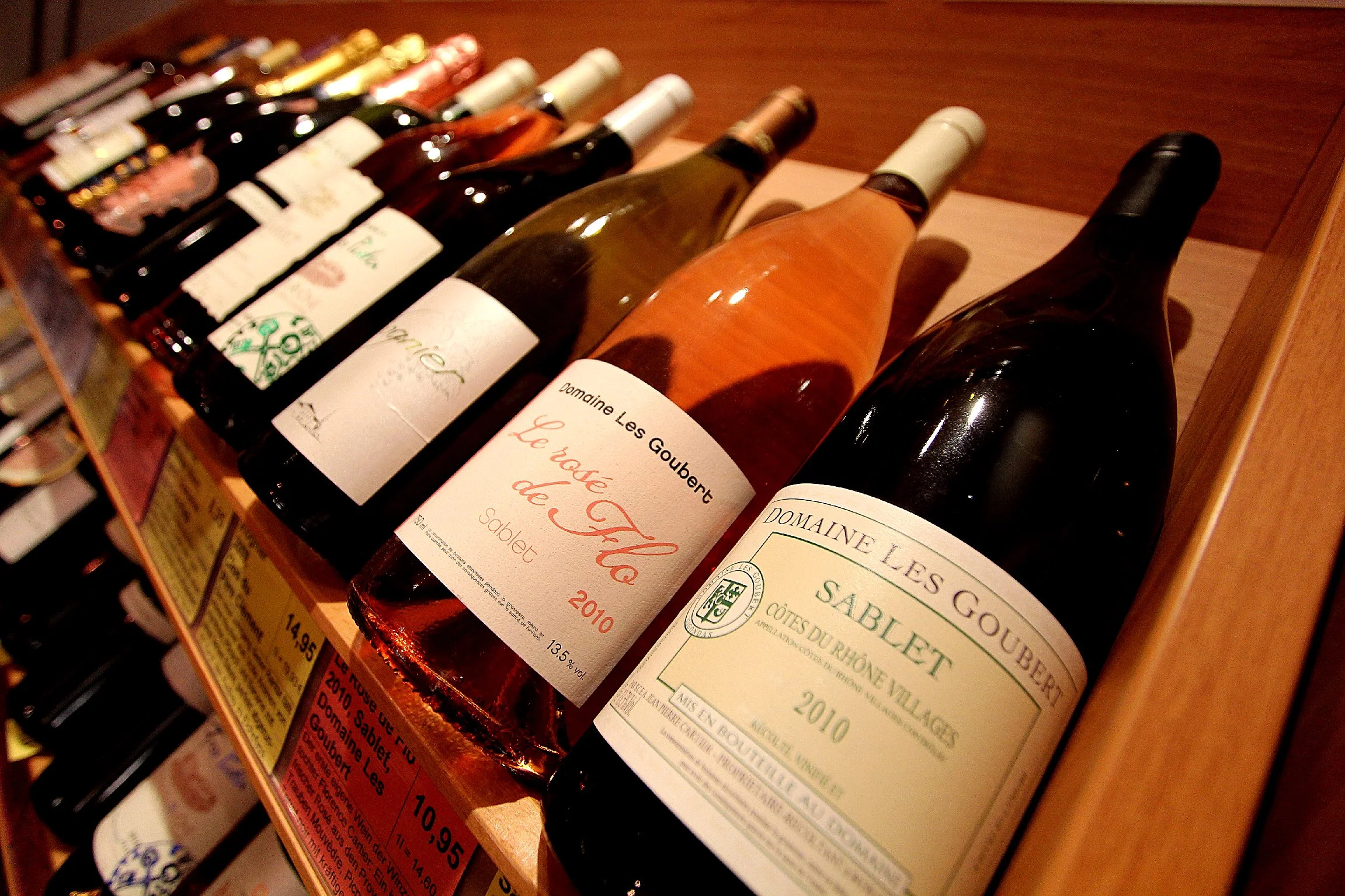 Verschiedene Flaschen Wein auf einem Weingeschäftsregal, darunter Château Sablé de la Loire aus dem Jahr 2010, Domaine Les Goubet Sablet aus dem Jahr 2010, und weitere Flaschen im Hintergrund.