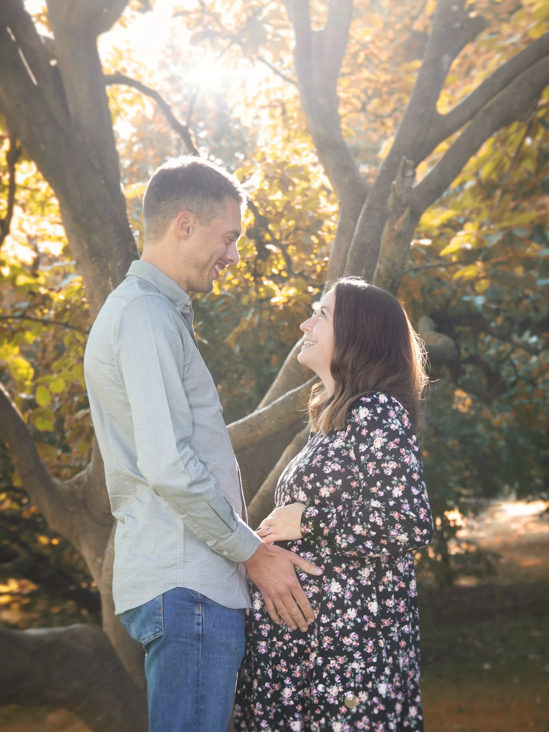 Ein glückliches Paar steht sich im Sonnenlicht bei Sonnenuntergang im Park gegenüber, hält sich an den Händen und blickt sich liebevoll an.