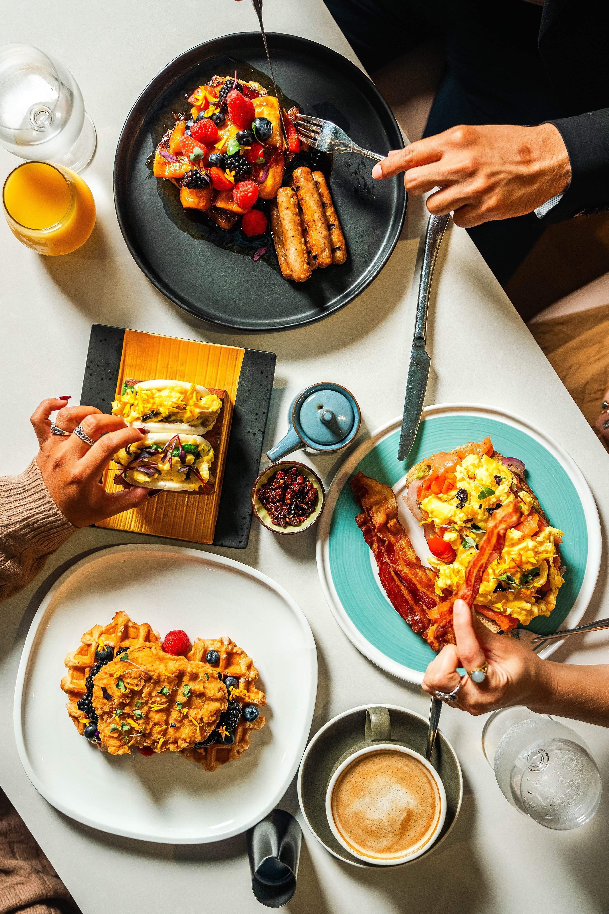 A table with various breakfast foods, including waffles topped with berries, scrambled eggs with bacon, and a pastry. Photo by Summerside Creative A Hotel Social Media & Creative Agency Serving Hospitality Brands