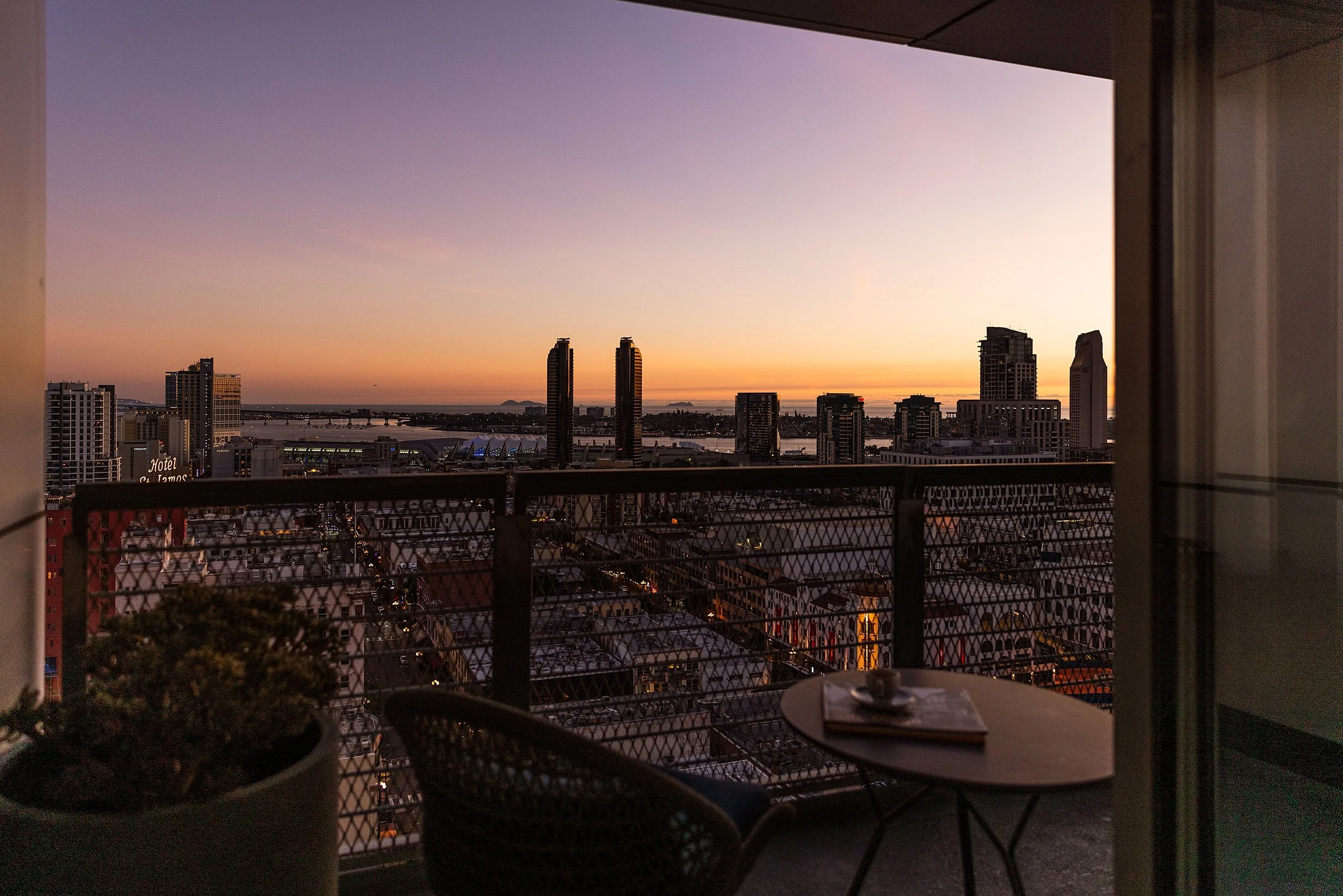 View from a balcony at sunset showing a city skyline with high-rise buildings, water, and a colorful sky. Photo by Summerside Creative A Hotel Social Media & Creative Agency Serving Hospitality Brands