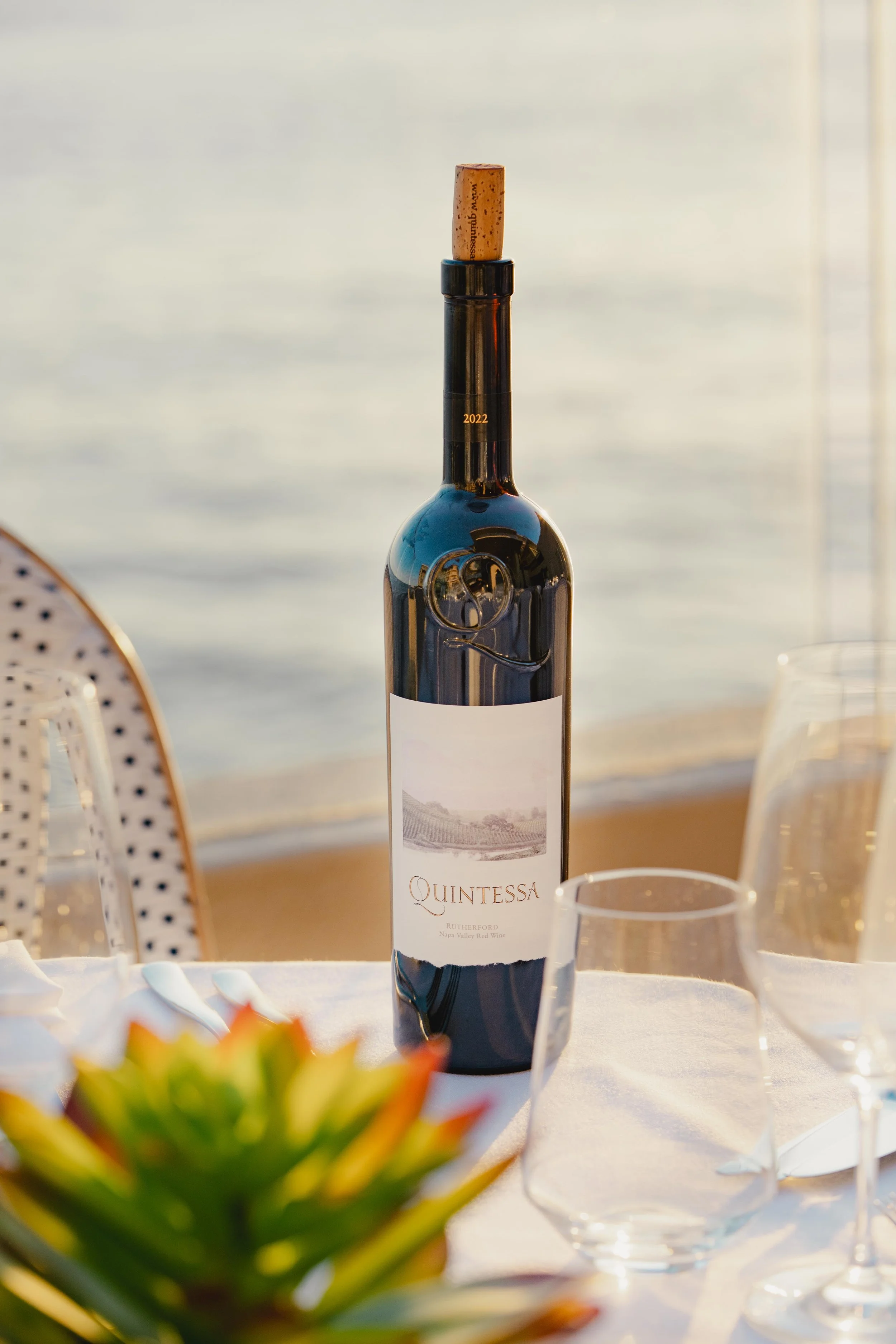 A bottle of Quintessa red wine with a cork inserted, placed on a table set for dining with glasses. Photo by Summerside Creative A Hotel Social Media & Creative Agency Serving Hospitality Brands