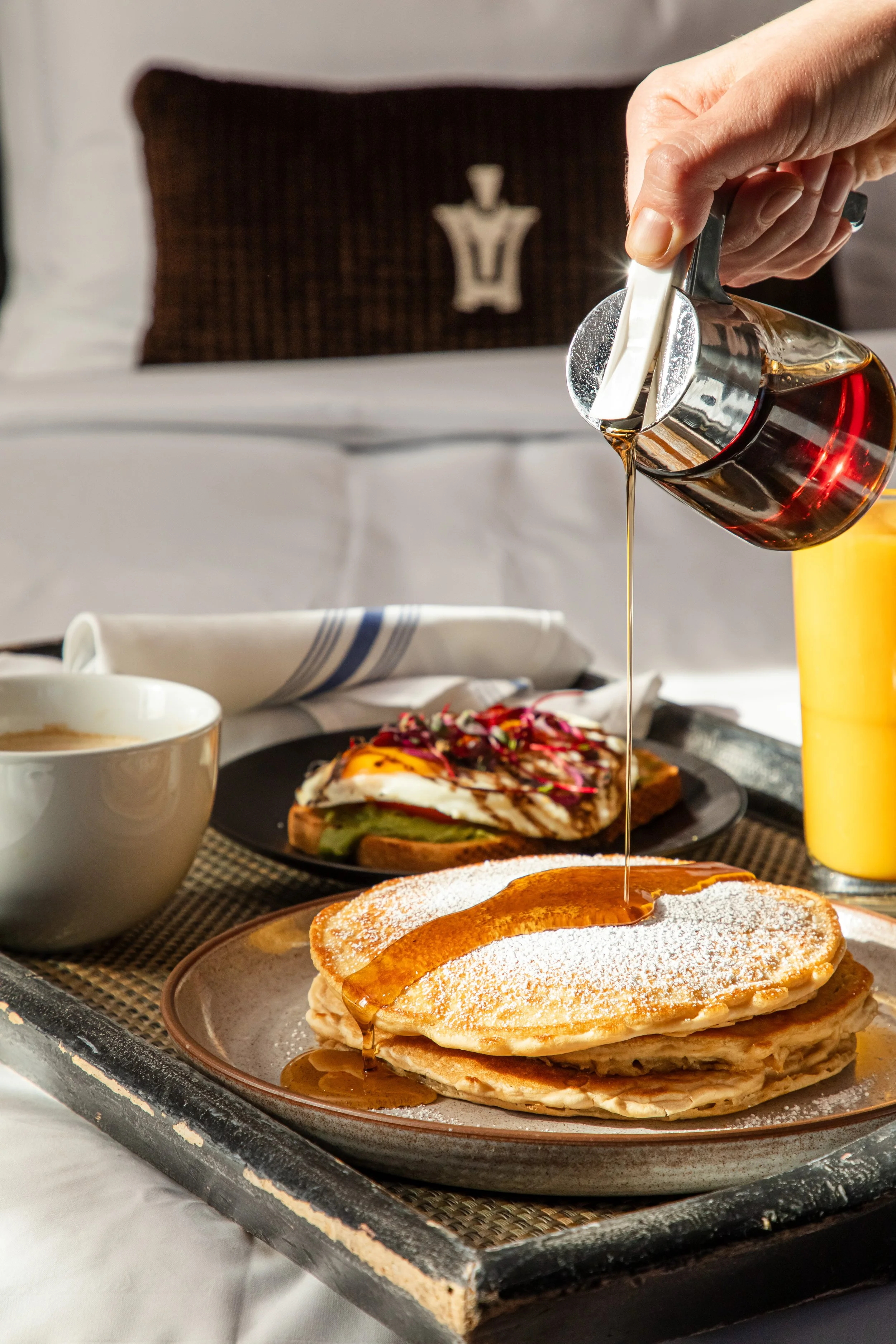 Pouring syrup onto a stack of pancakes on a plate. Photo by Summerside Creative A Hotel Social Media & Creative Agency Serving Hospitality Brands