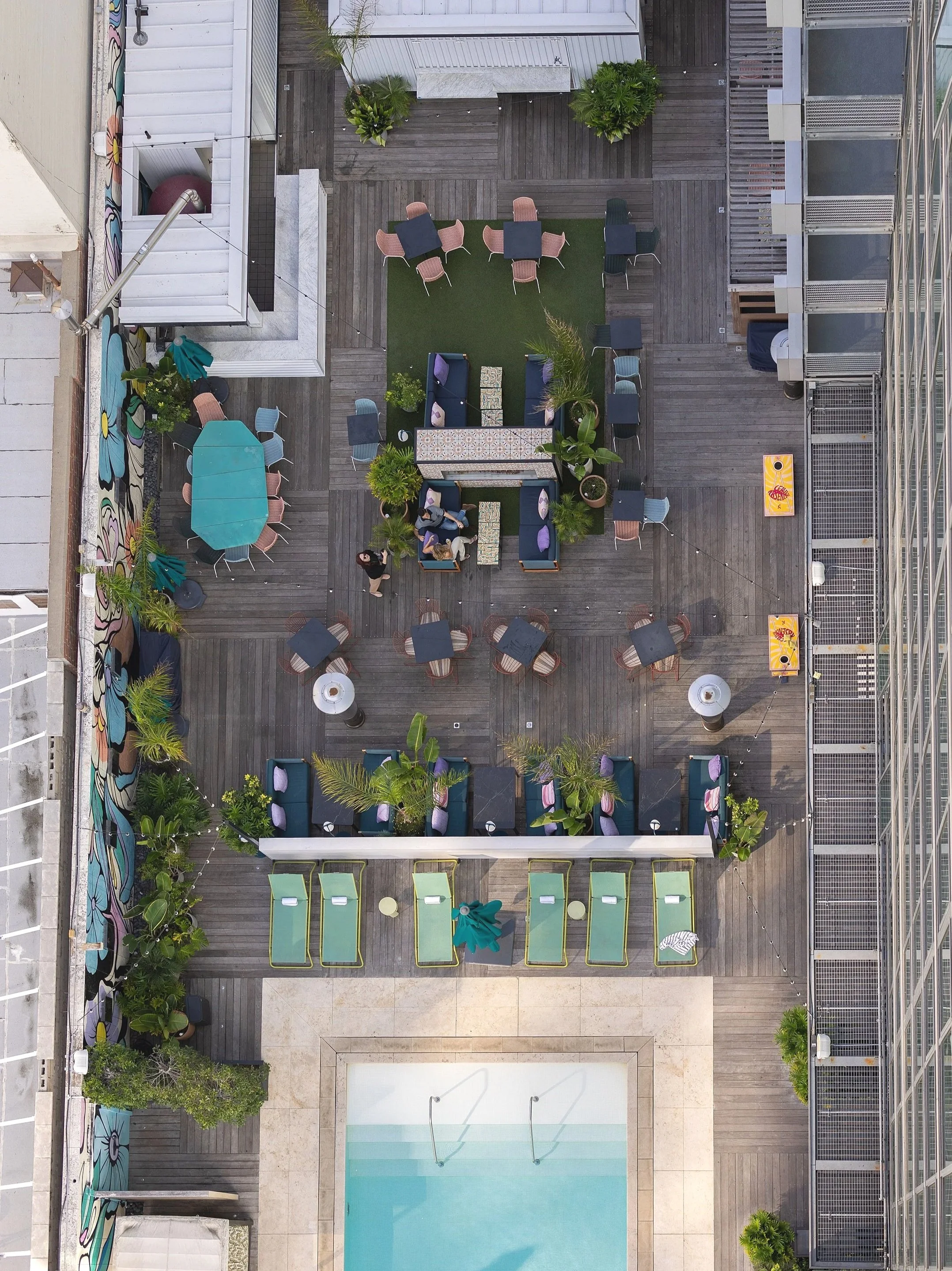 A rooftop patio with various seating areas, including sun loungers, tables and chairs, near a swimming pool, decorated with potted plants and colorful murals. Photo by Summerside Creative A Hotel Social Media & Creative Agency Serving Hospitality Bra