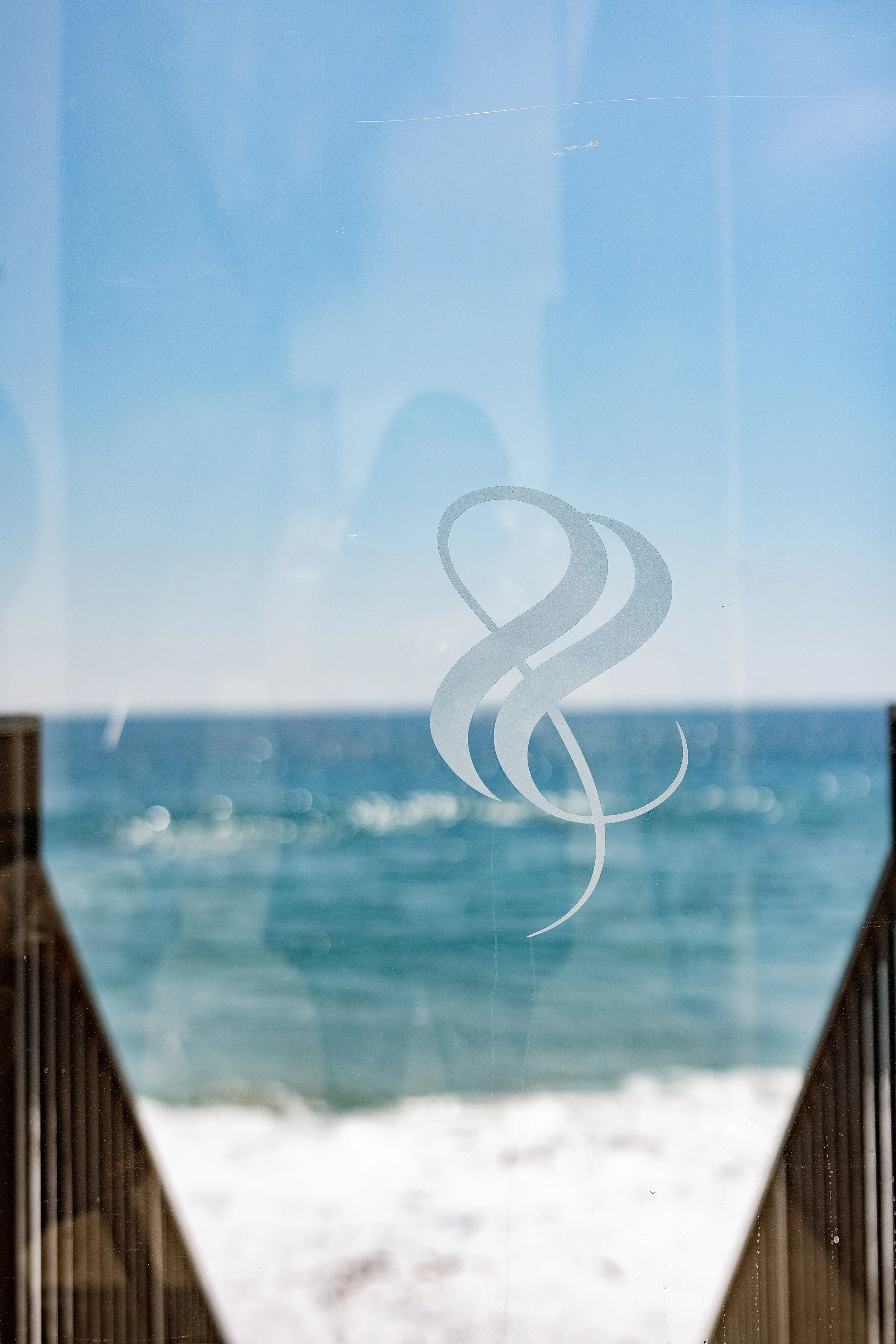 A glass window with a medical symbol decal, showing an ocean view with blue water and a clear sky in the background. Photo by Summerside Creative A Hotel Social Media & Creative Agency Serving Hospitality Brands