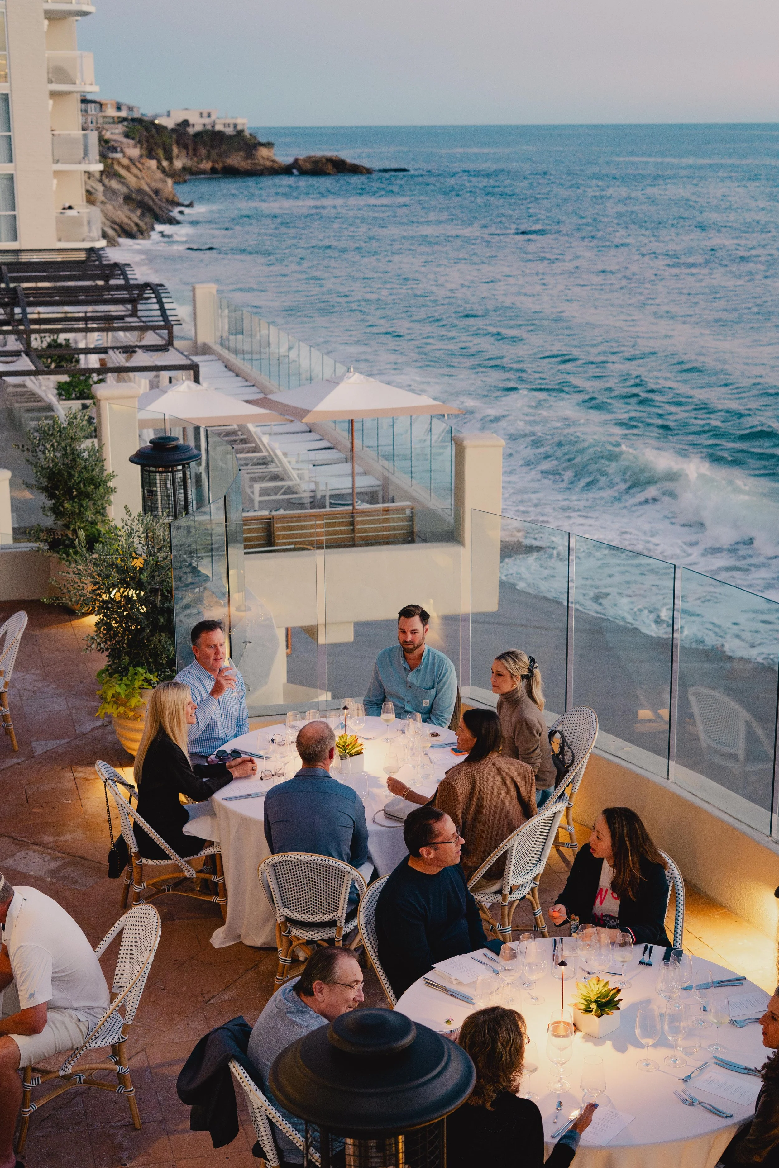 People dining at outdoor restaurant overlooking the ocean during sunset, with beach chairs and umbrellas on the balcony. Photo by Summerside Creative A Hotel Social Media & Creative Agency Serving Hospitality Brands