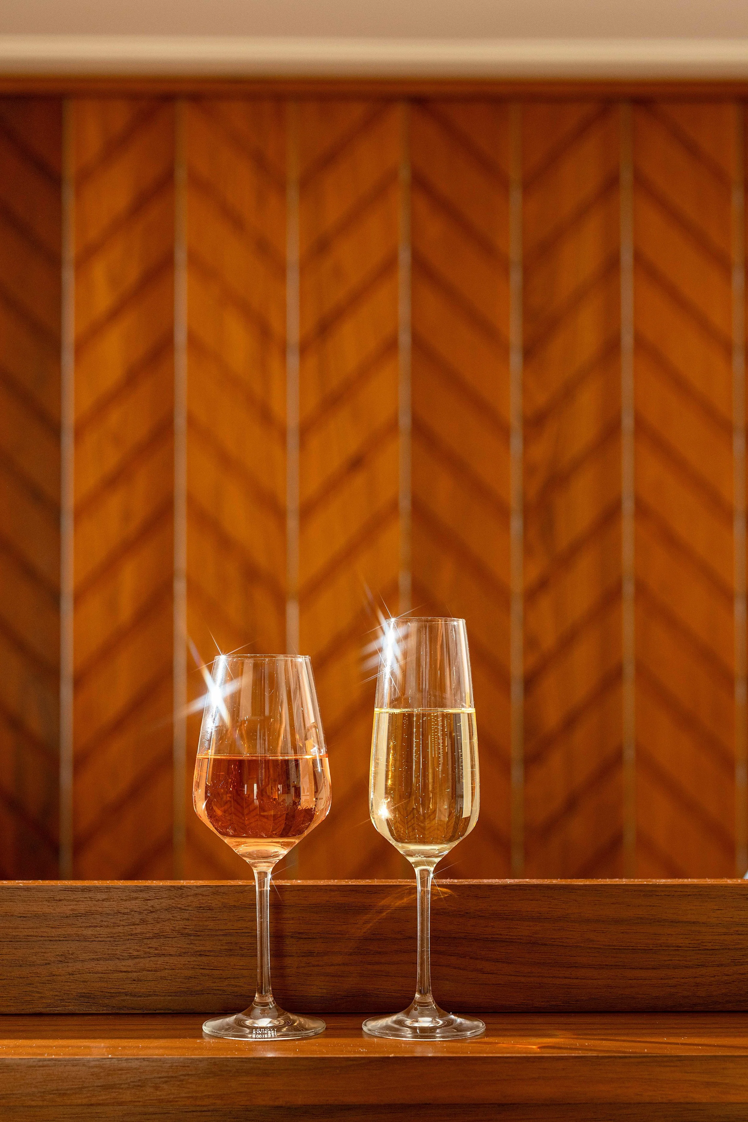 Two glasses of sparkling wine, one rosé and one white, on a wooden surface against a decorative wooden wall. Photo by Summerside Creative A Hotel Social Media & Creative Agency Serving Hospitality Brands