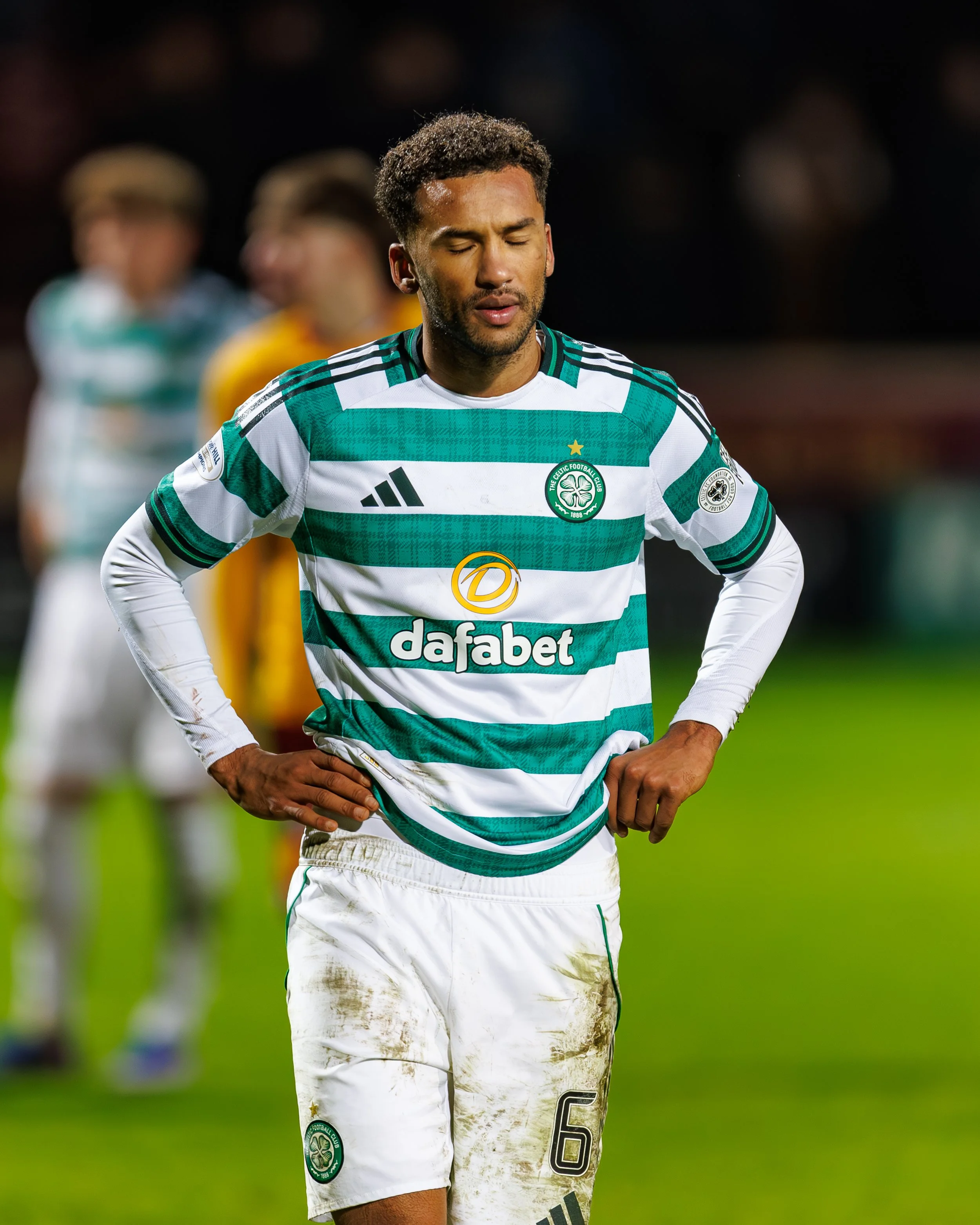Soccer player wearing a green and white striped jersey with 'dafabet' logo, standing on a field with a distressed look and hands on hips.