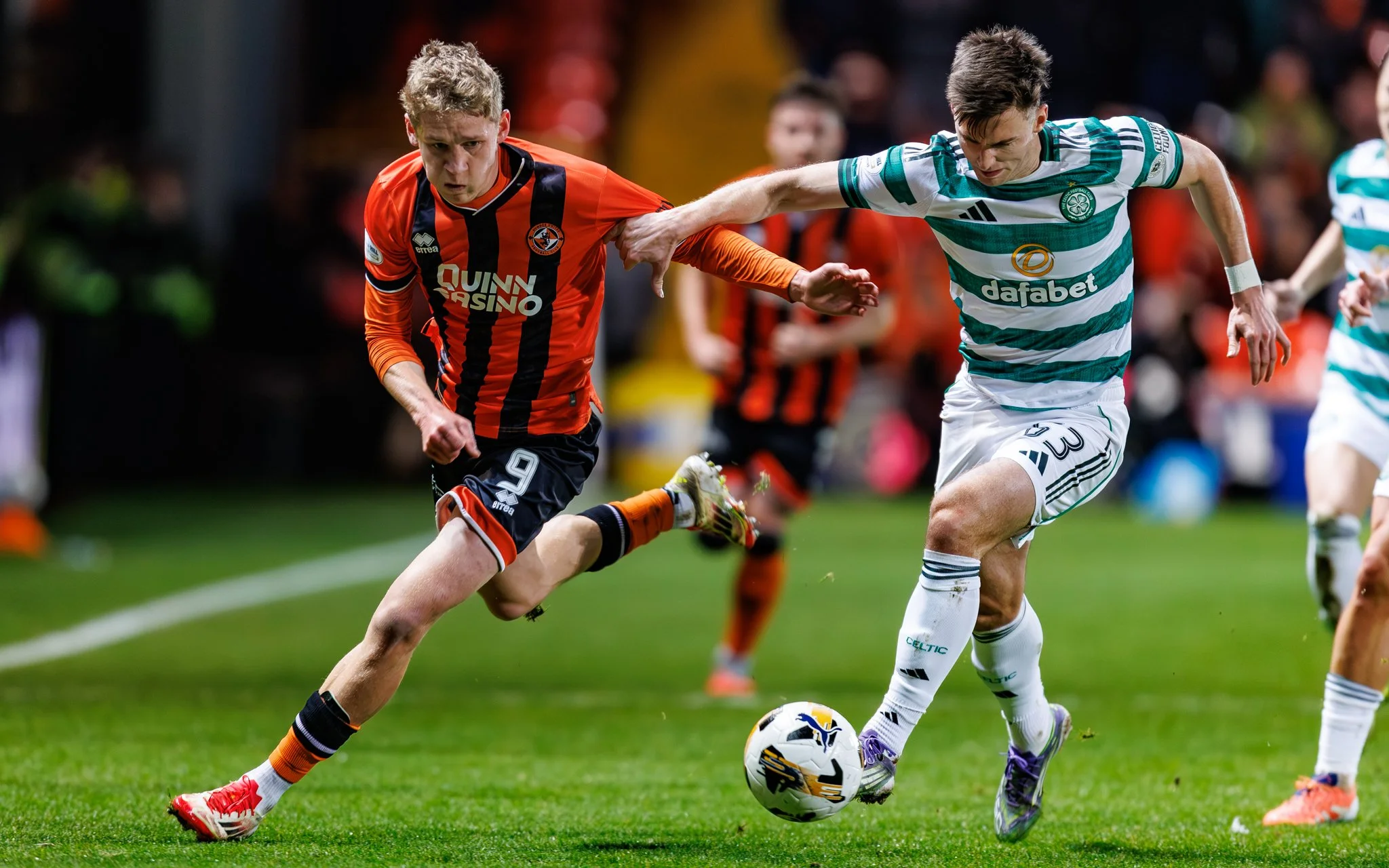 Two soccer players competing for the ball during a match, one wearing an orange and black uniform and the other in a green and white striped jersey.