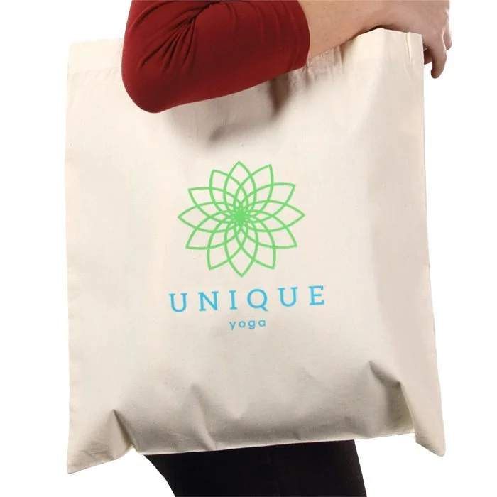 A person holding a white tote bag with a green geometric flower design and the words "UNIQUE yoga" printed on it.