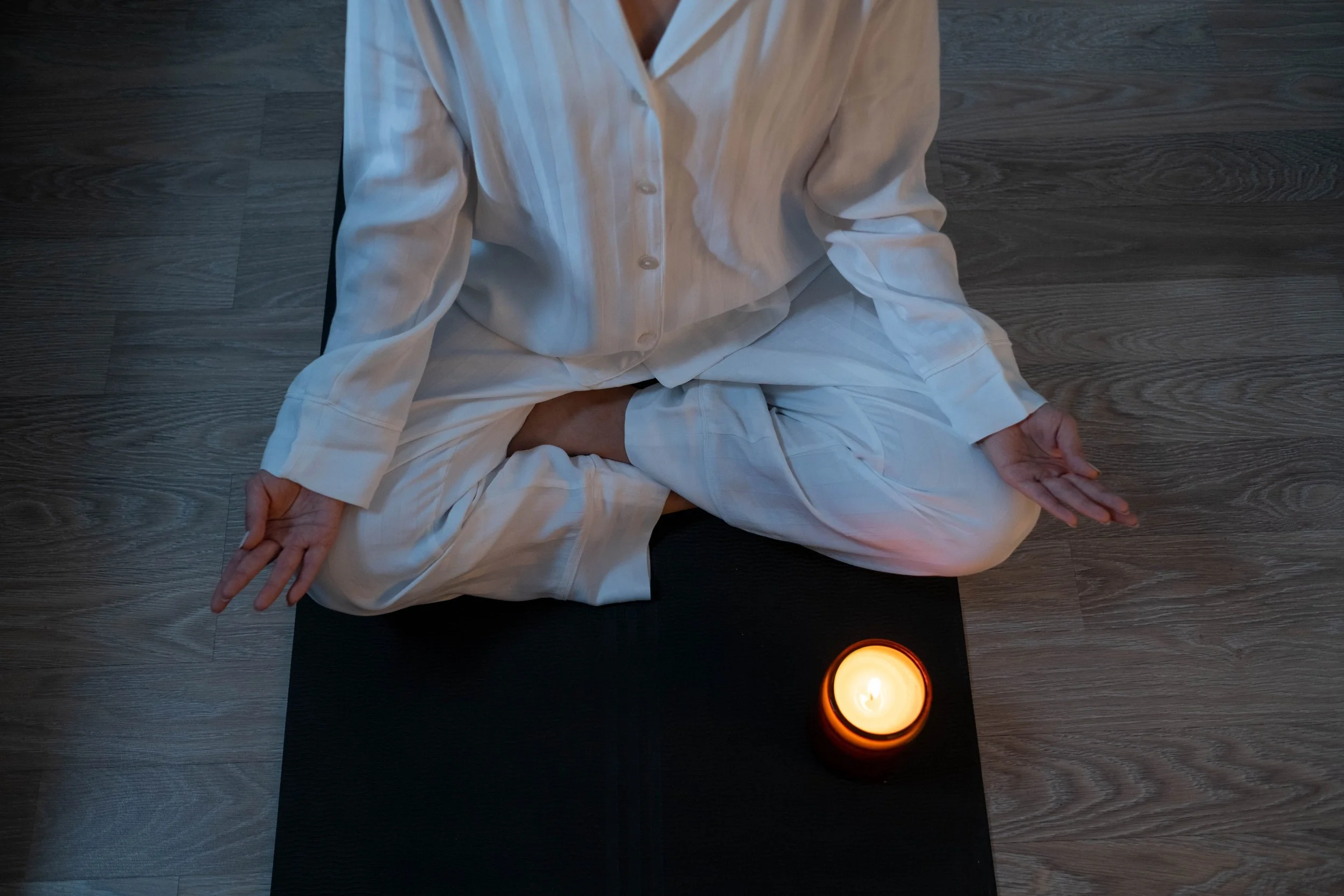 A person seated in a yoga pose with a candle in front of them