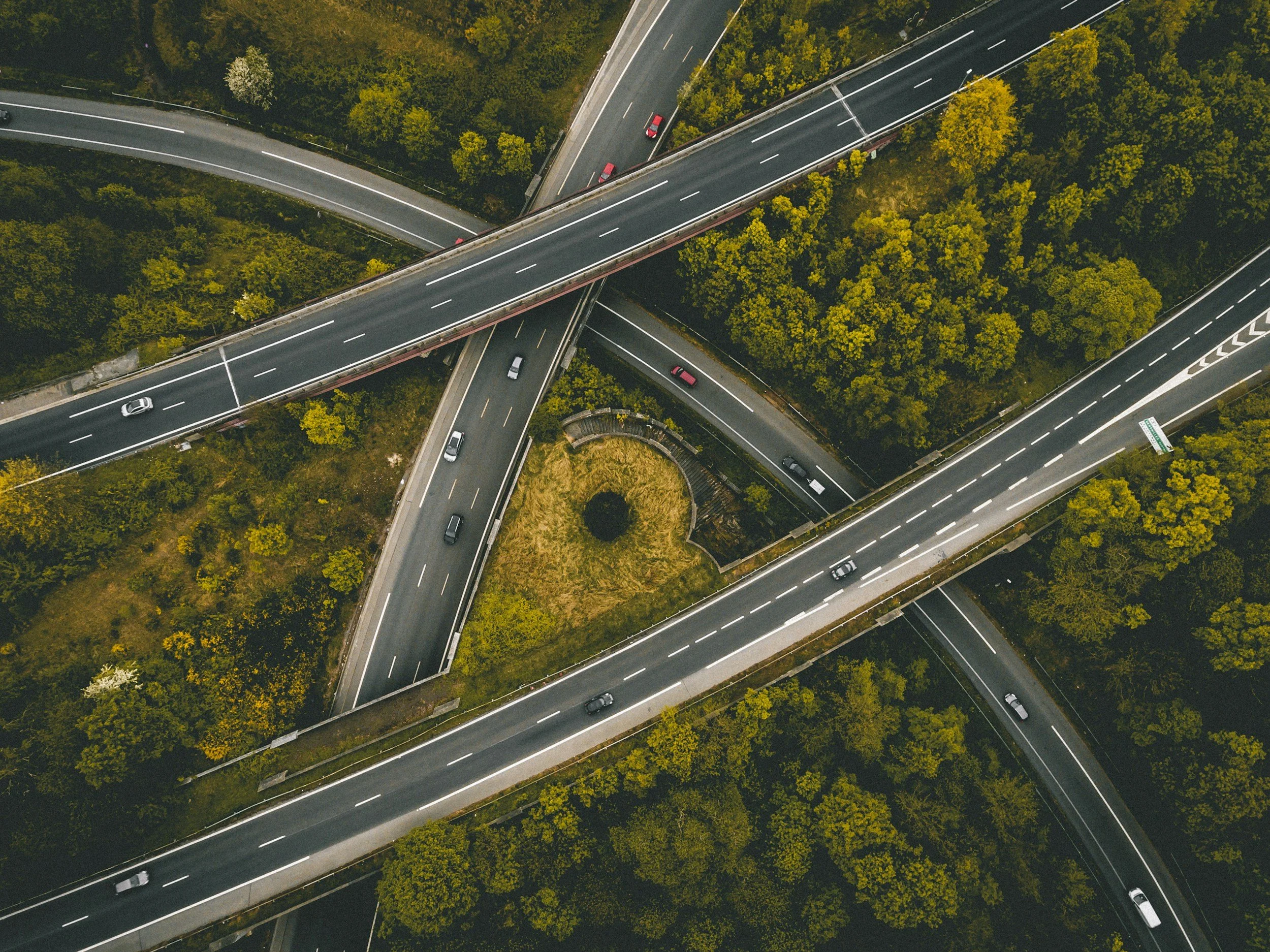 An aerial view of a multi-level highway interchange with cars traveling in various directions, surrounded by lush green trees.