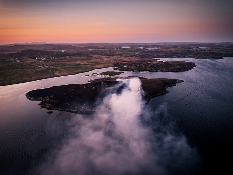 Aerial view of a loch and islands in the Pairc, Kinloch and North Harris area, during sunset, with mist rising over the water and a distant landscape in the background.