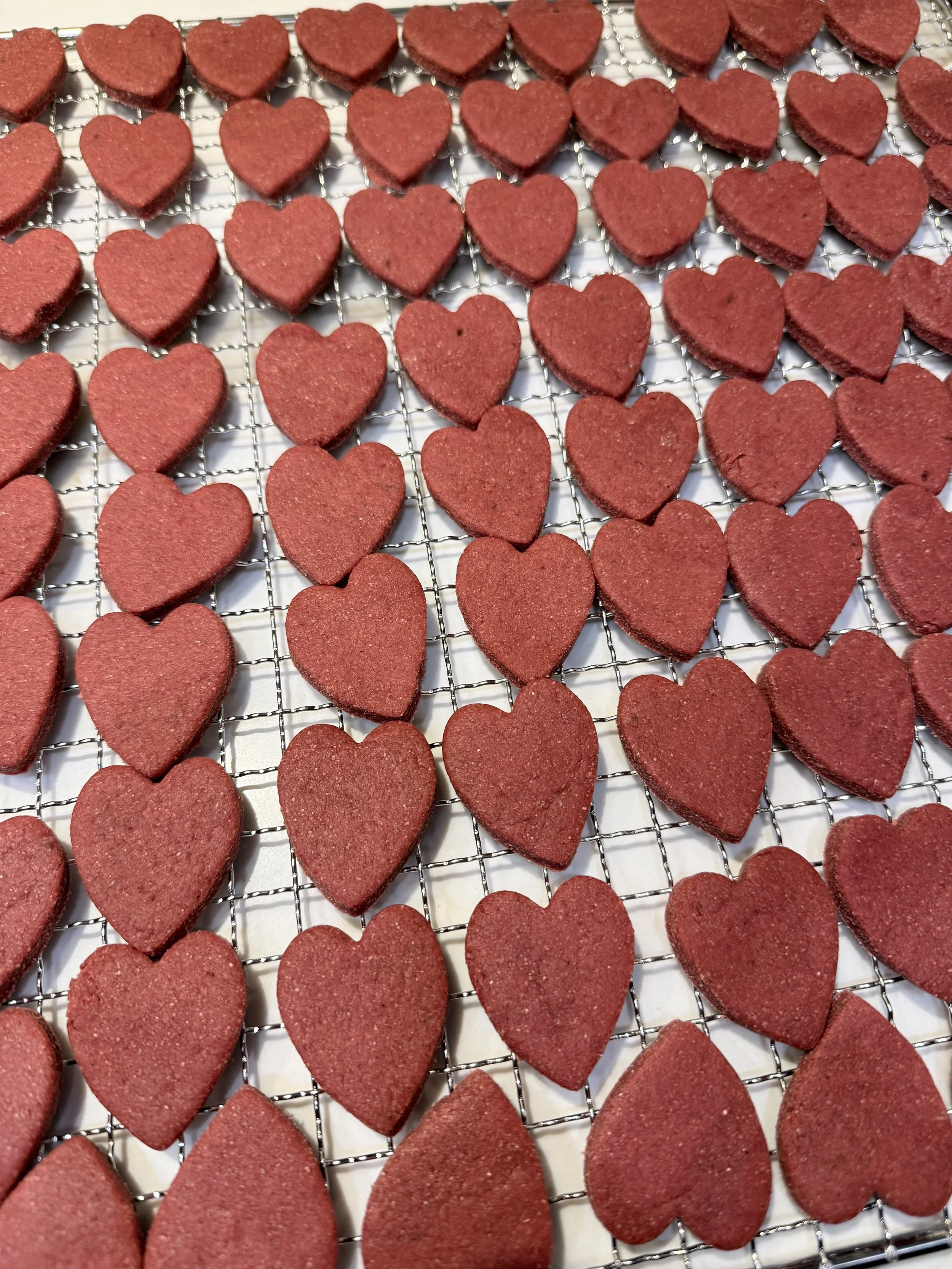 Red heart-shaped cookies cooling on a wire rack.