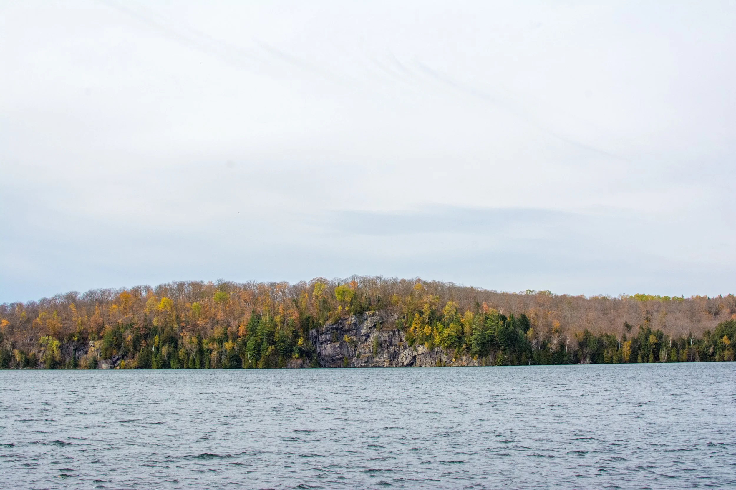 Scenic view of a lake with a tree-covered island in the distance, under a cloudy sky.