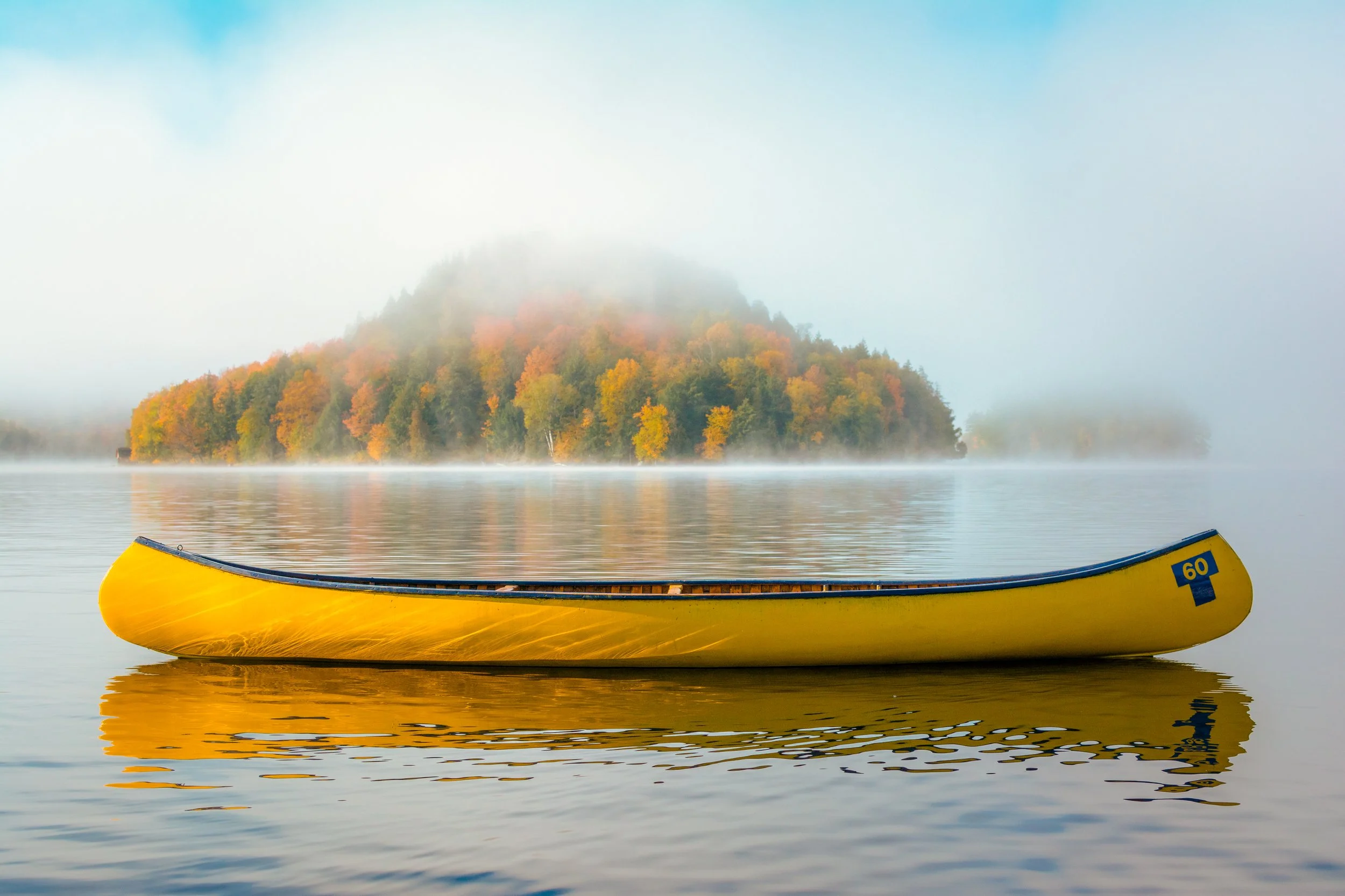 Yellow canoe floating on calm water with misty fog and a forested hill in the background.