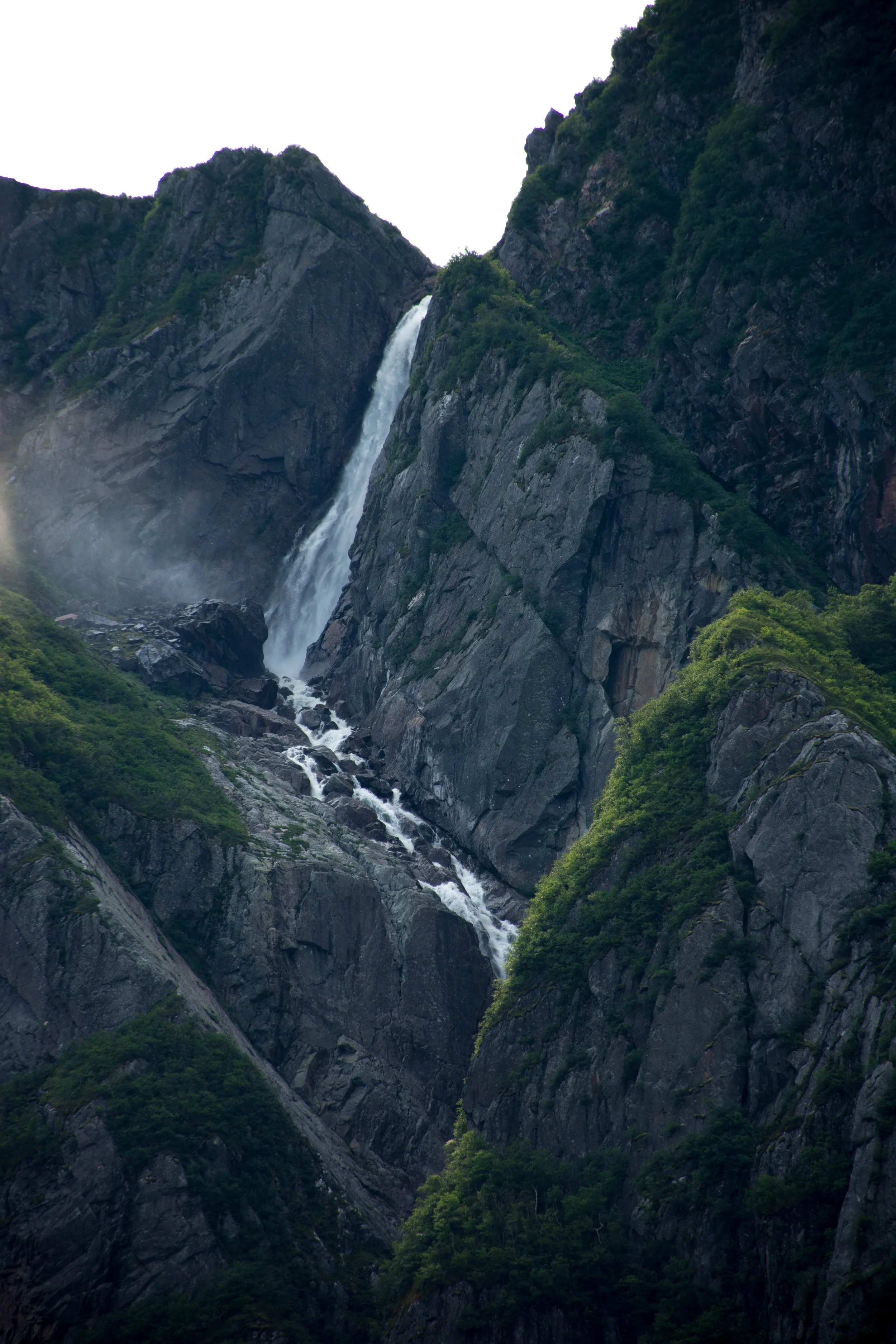 A waterfall cascading down steep, rocky mountain cliffs surrounded by lush green trees.