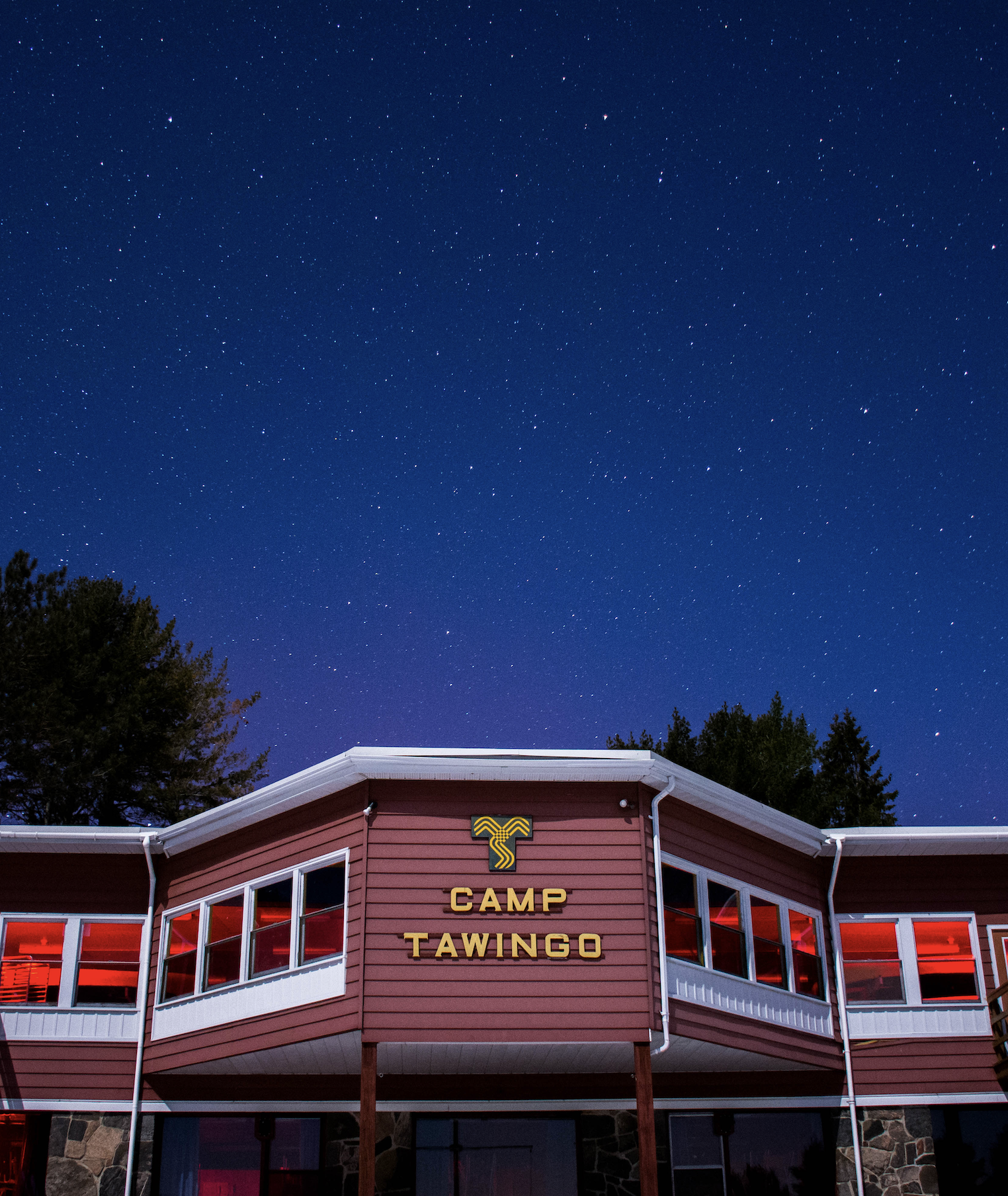 A building with a sign that reads 'Camp Tawingo', under a starry night sky.