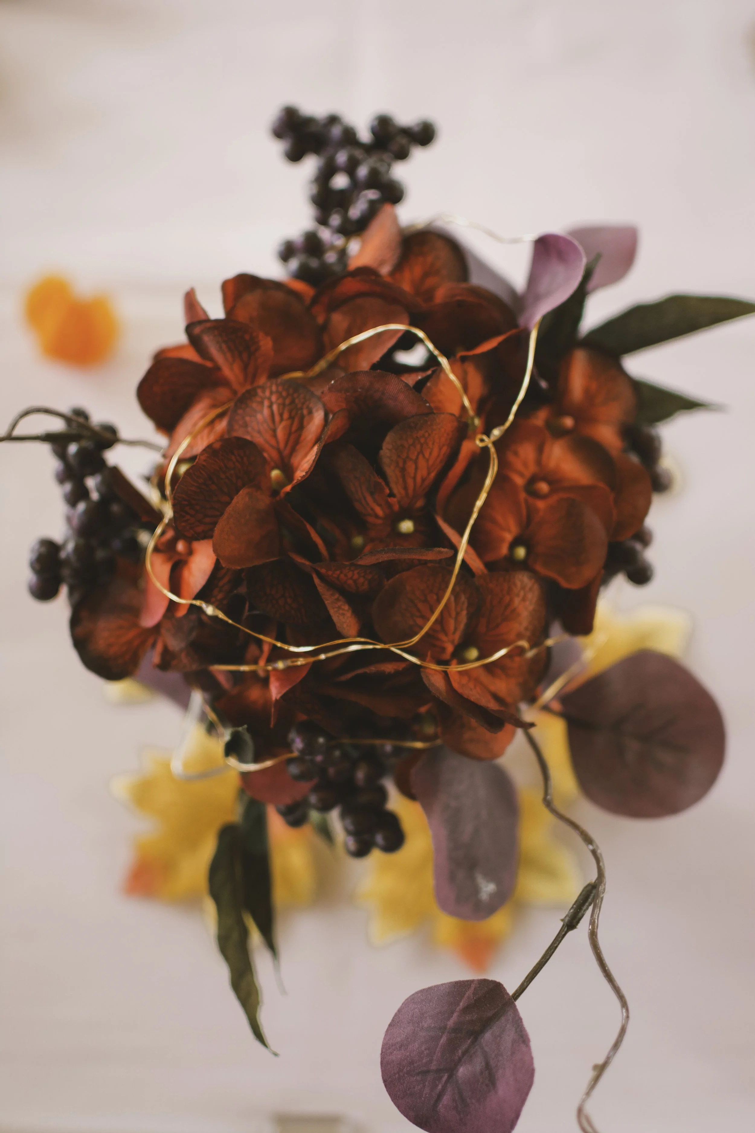 A bouquet of red flowers with dark purple berries, green and purple leaves, and gold wire accents.