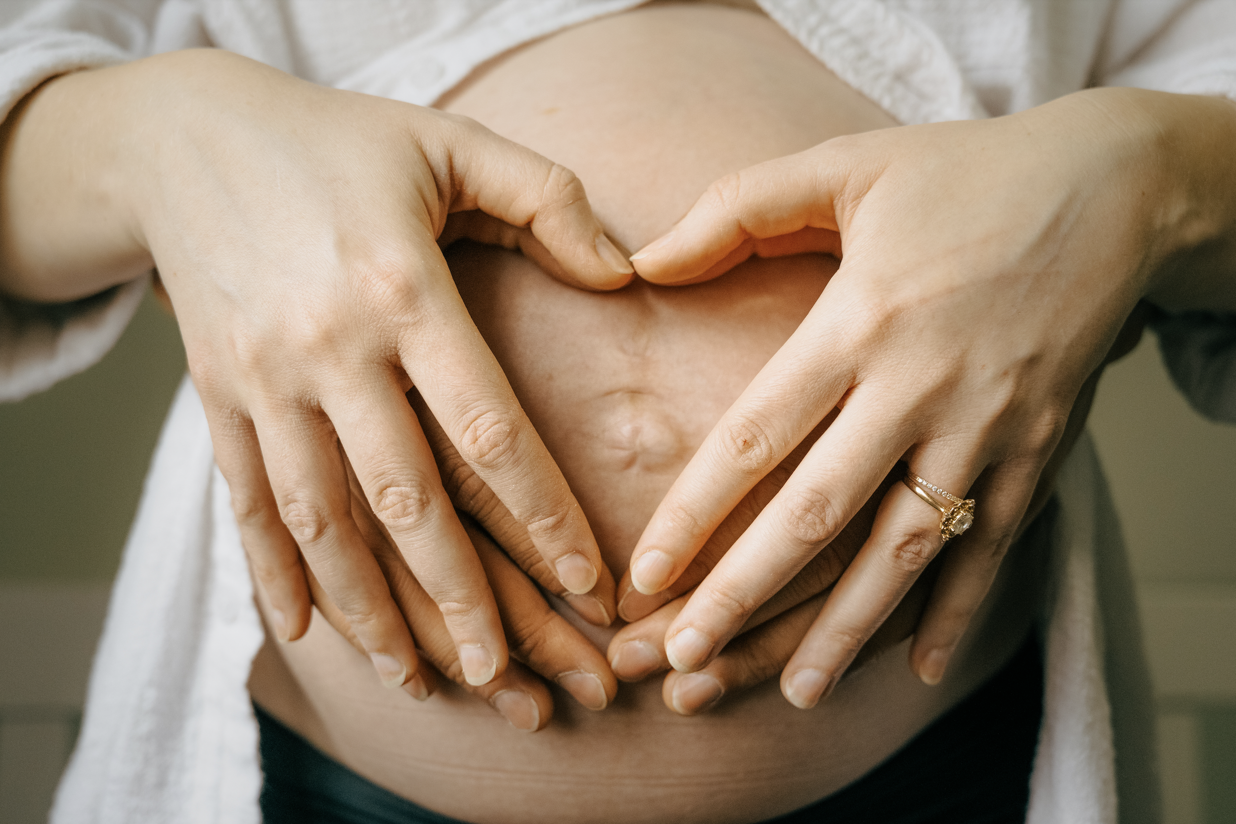 Two women forming a heart shape with their hands over a pregnant belly.