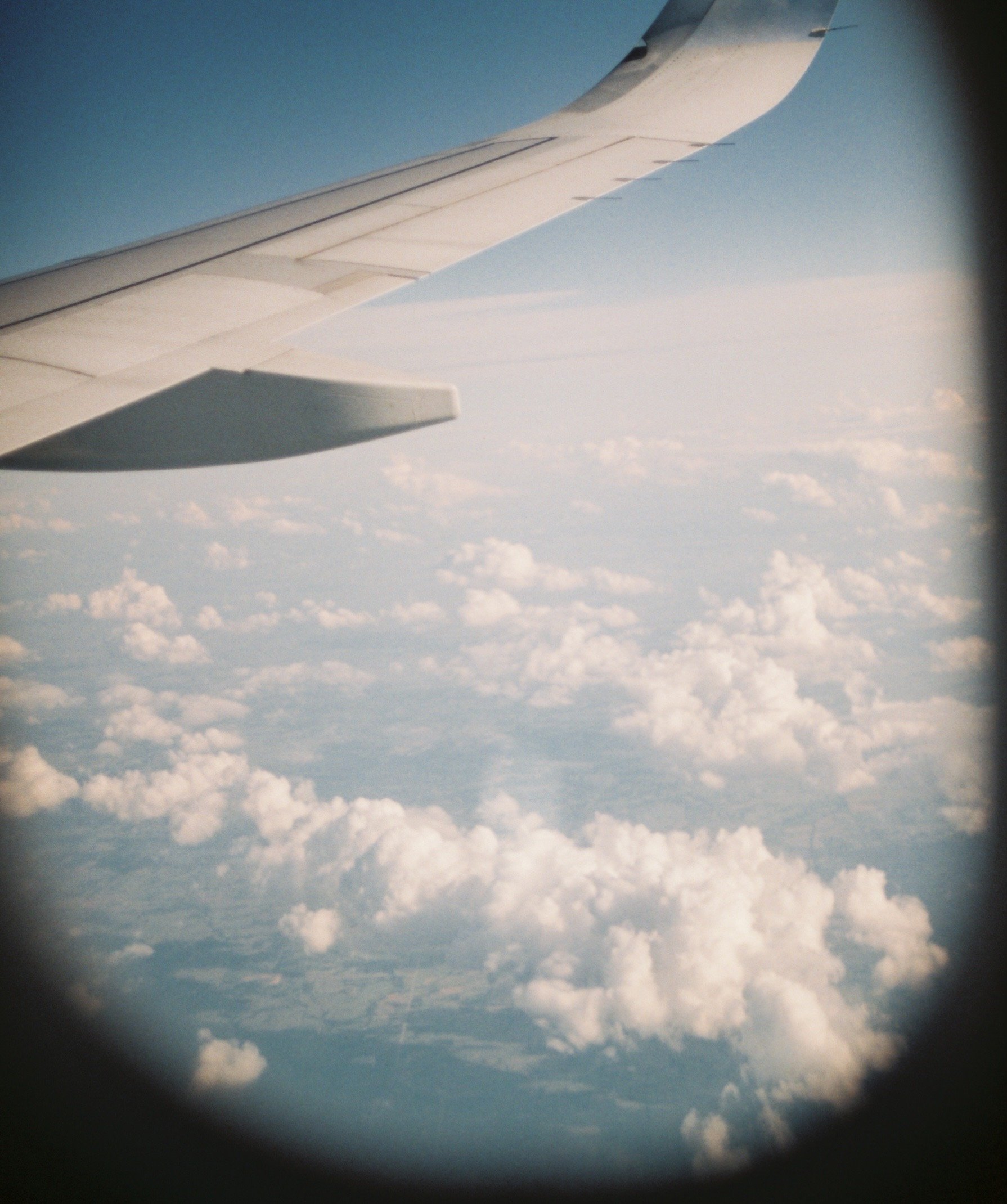View of an airplane wing from a window, flying above clouds in the sky.