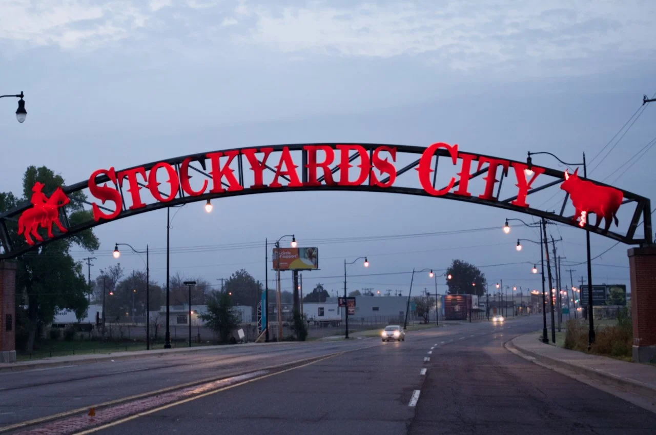 Street view of the Stockton City sign with red neon lights and red cow and horse silhouettes, illuminated in a dusk setting.