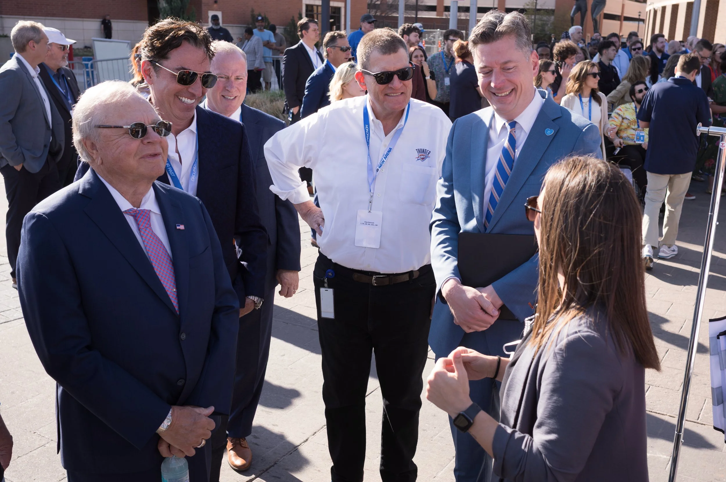 A group of professional people in suits and sunglasses having a conversation outdoors at a crowded event.