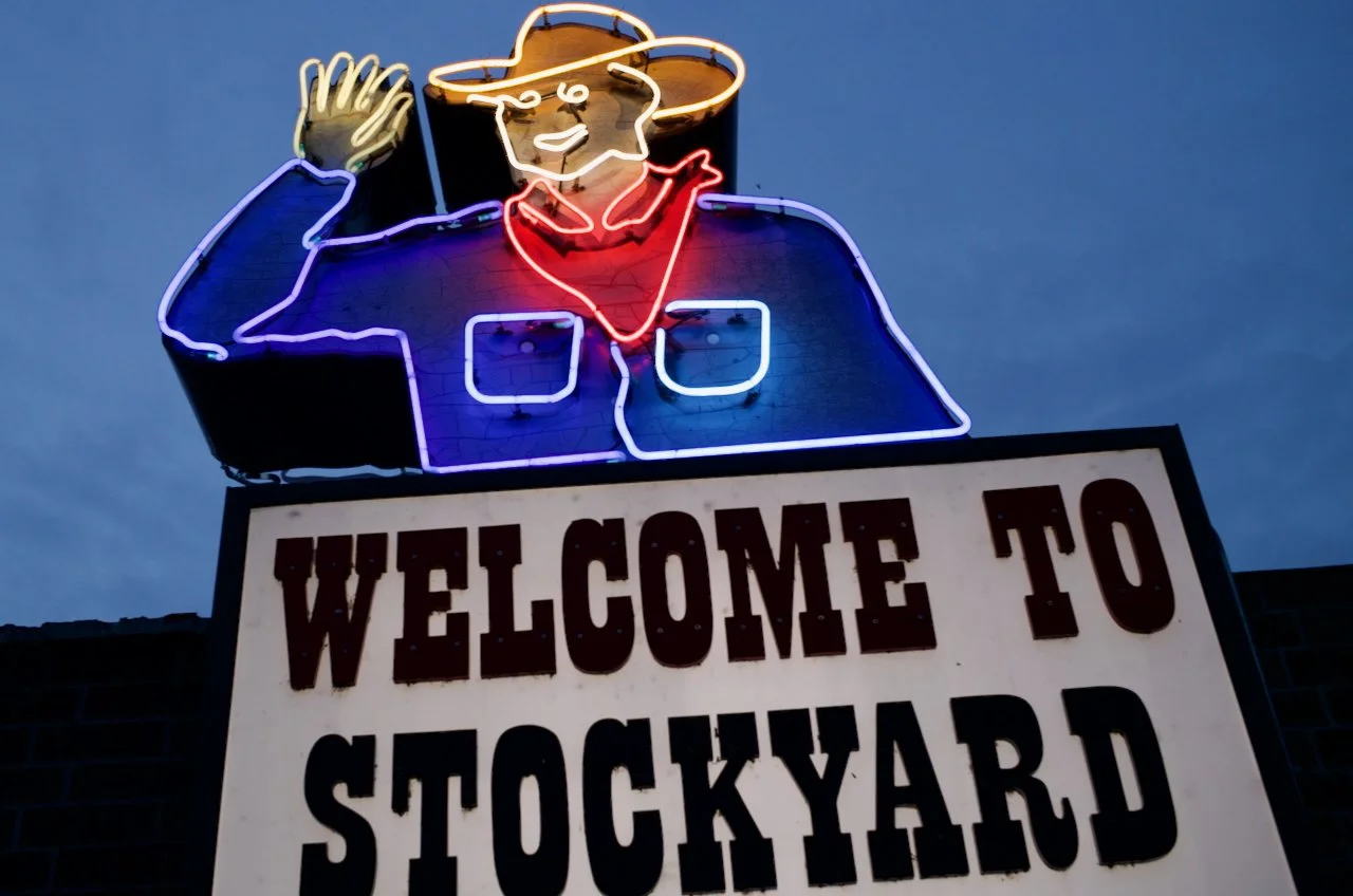 Neon sign of a cowboy waving, above a sign that says "Welcome to Stockyard".