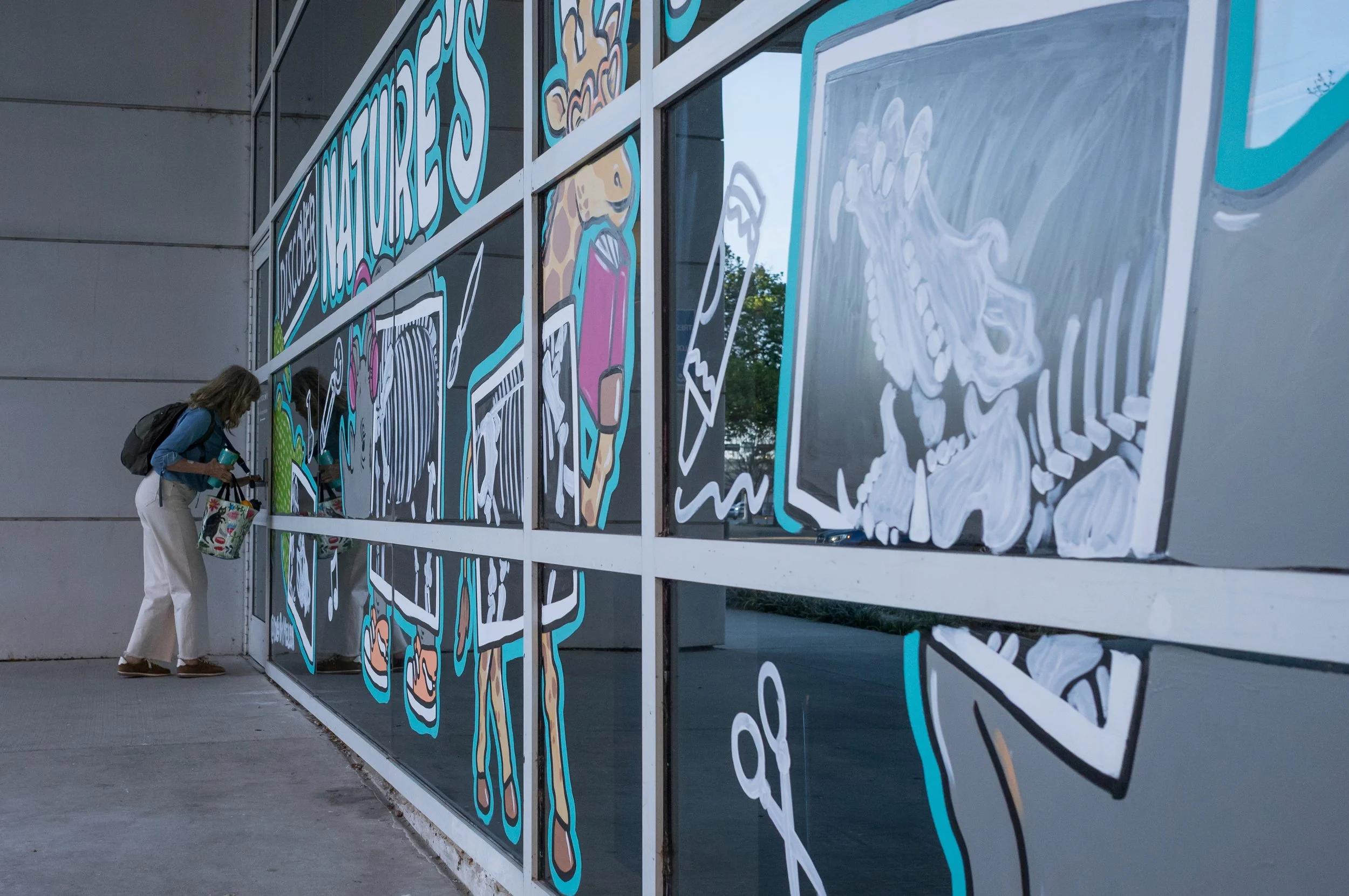 A woman observing a colorful mural on a glass wall, featuring animals and nature-themed illustrations.