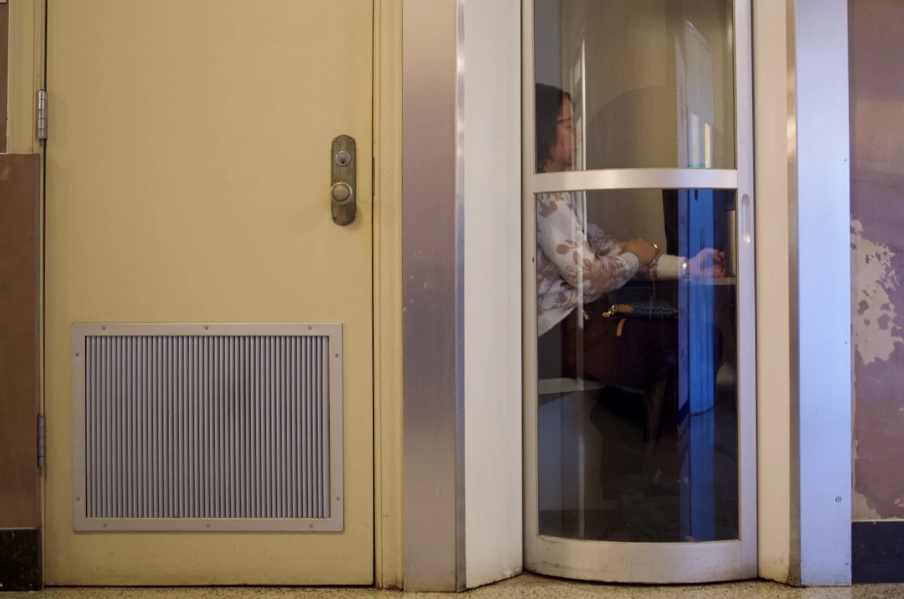 A woman sitting at a table in a glass-walled room, using a laptop.