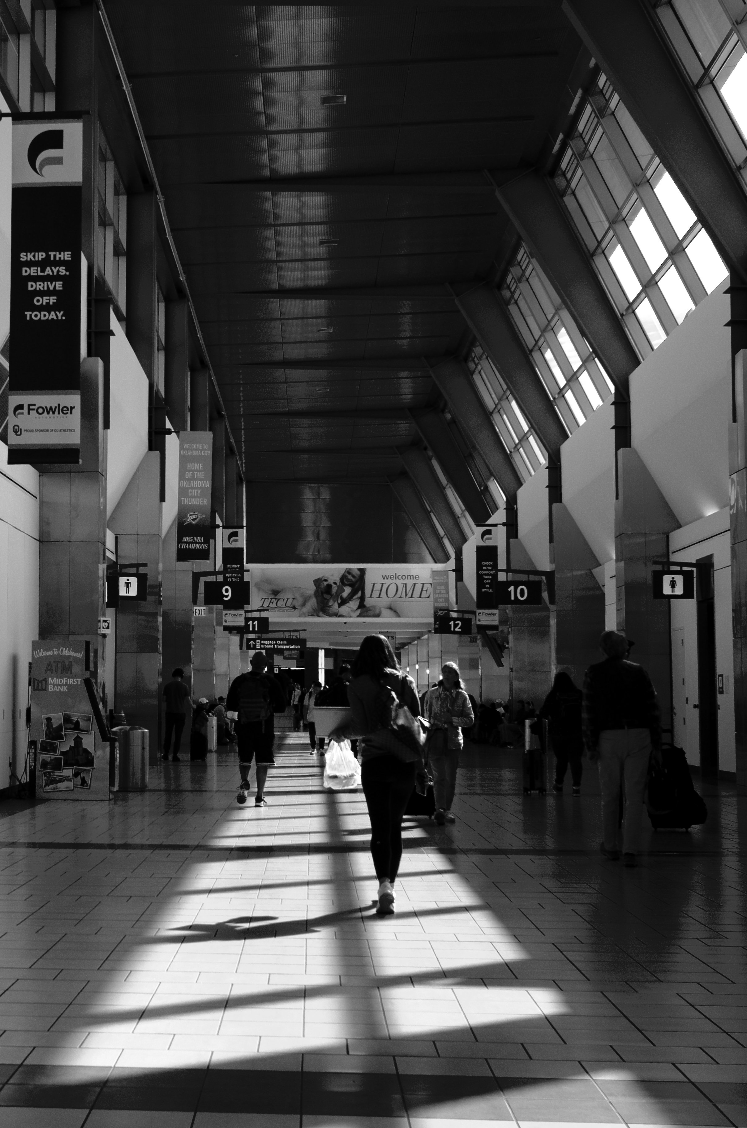 People walking through a spacious airport terminal with high ceilings and large windows, black and white photo.