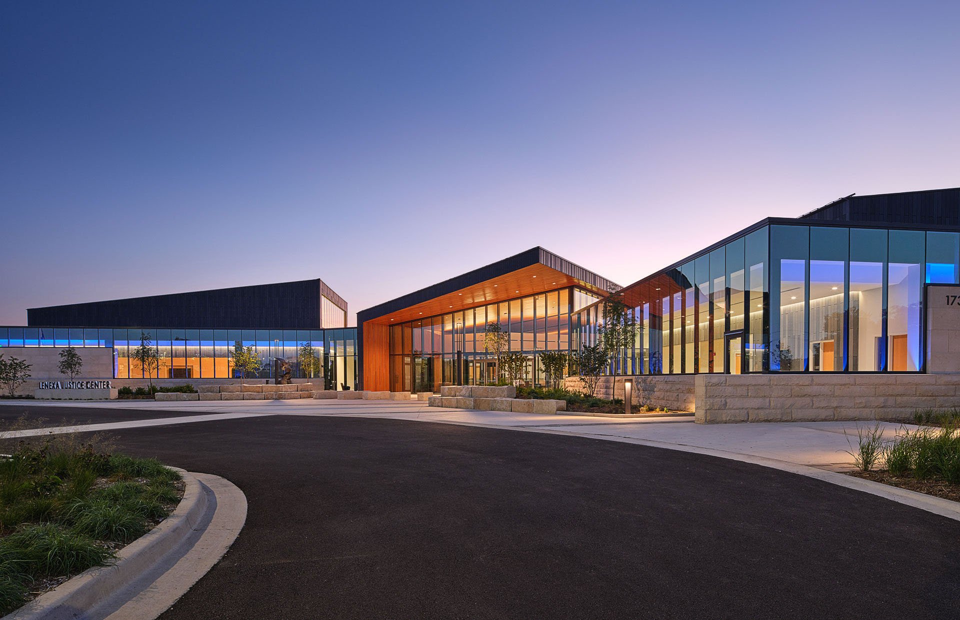 Modern justice center building with large glass windows and landscaped surroundings at dusk.